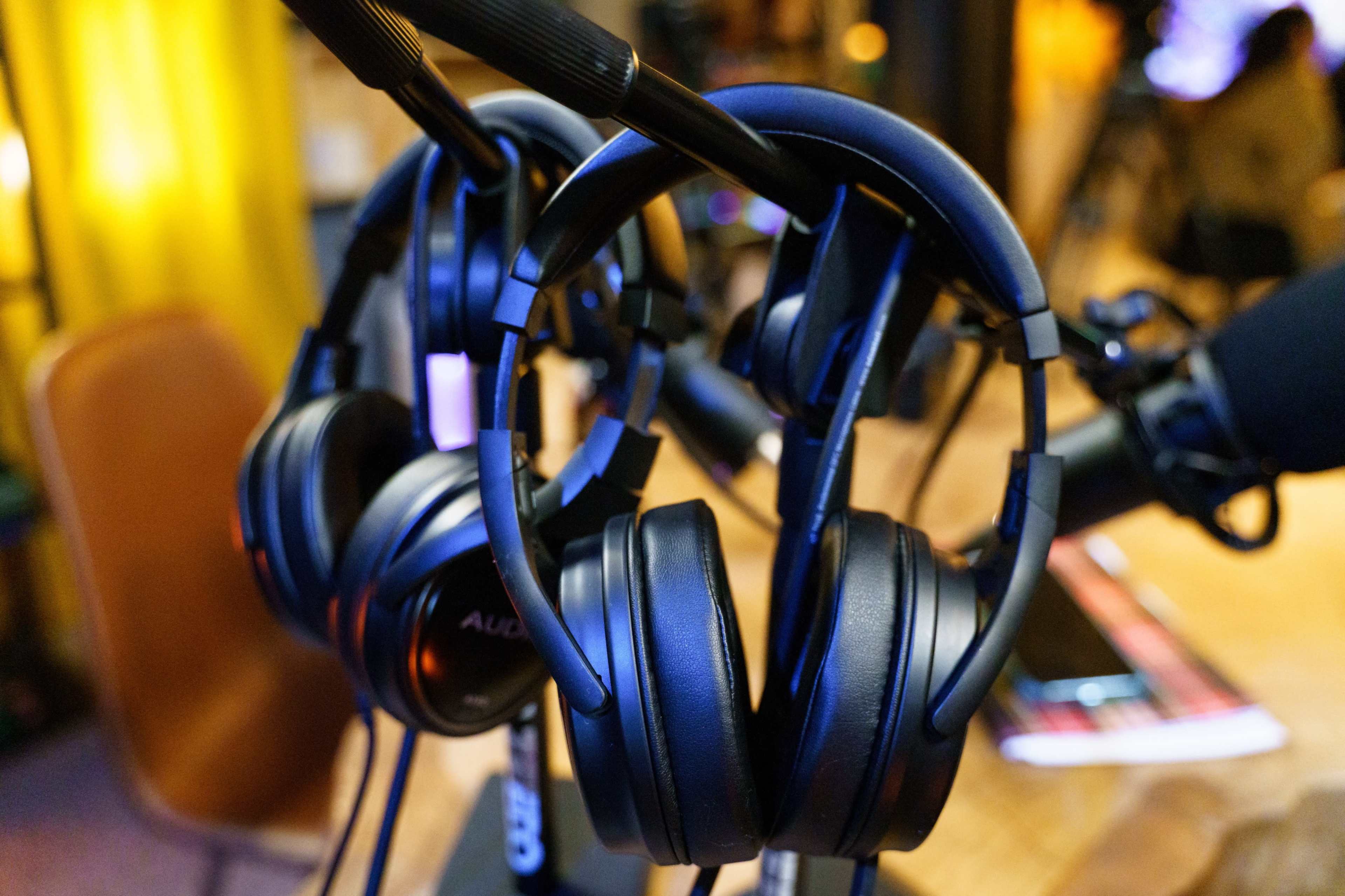 Several pairs of black headphones hanging on a stand, with warm lighting in the background.
