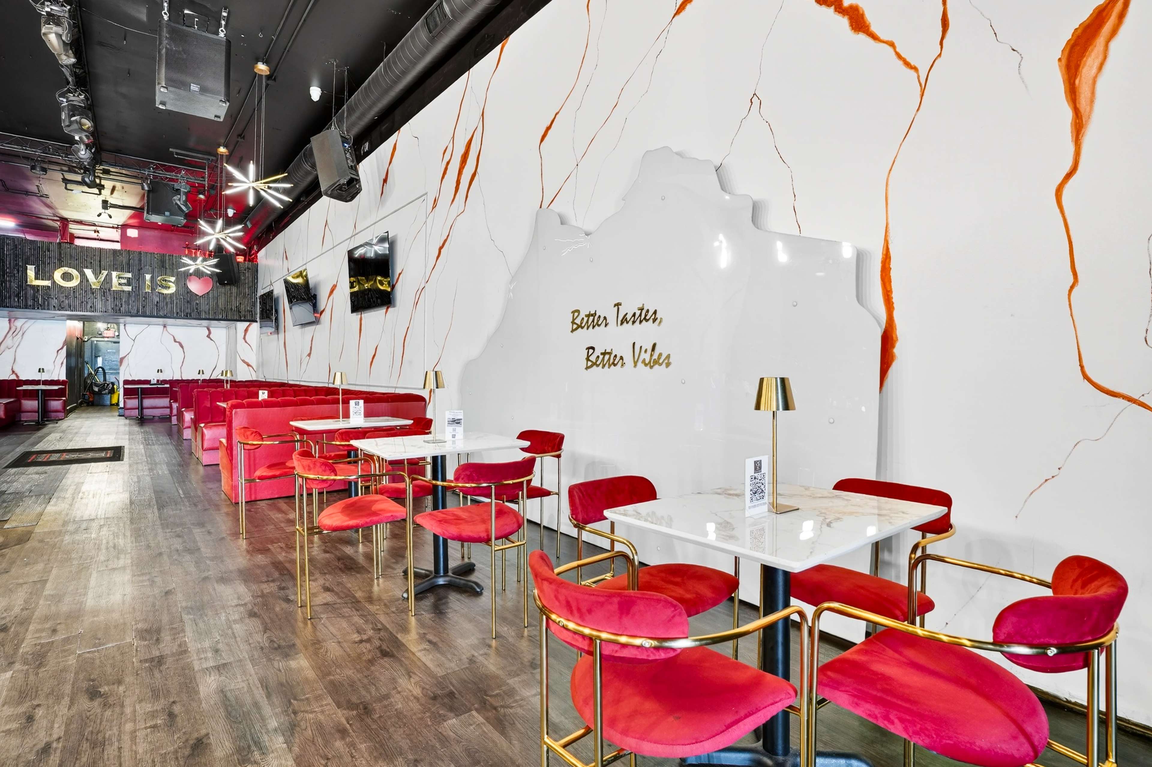 The image shows a modern restaurant interior with red velvet seating, marble tables, and a decorative wall featuring orange and white patterns.
