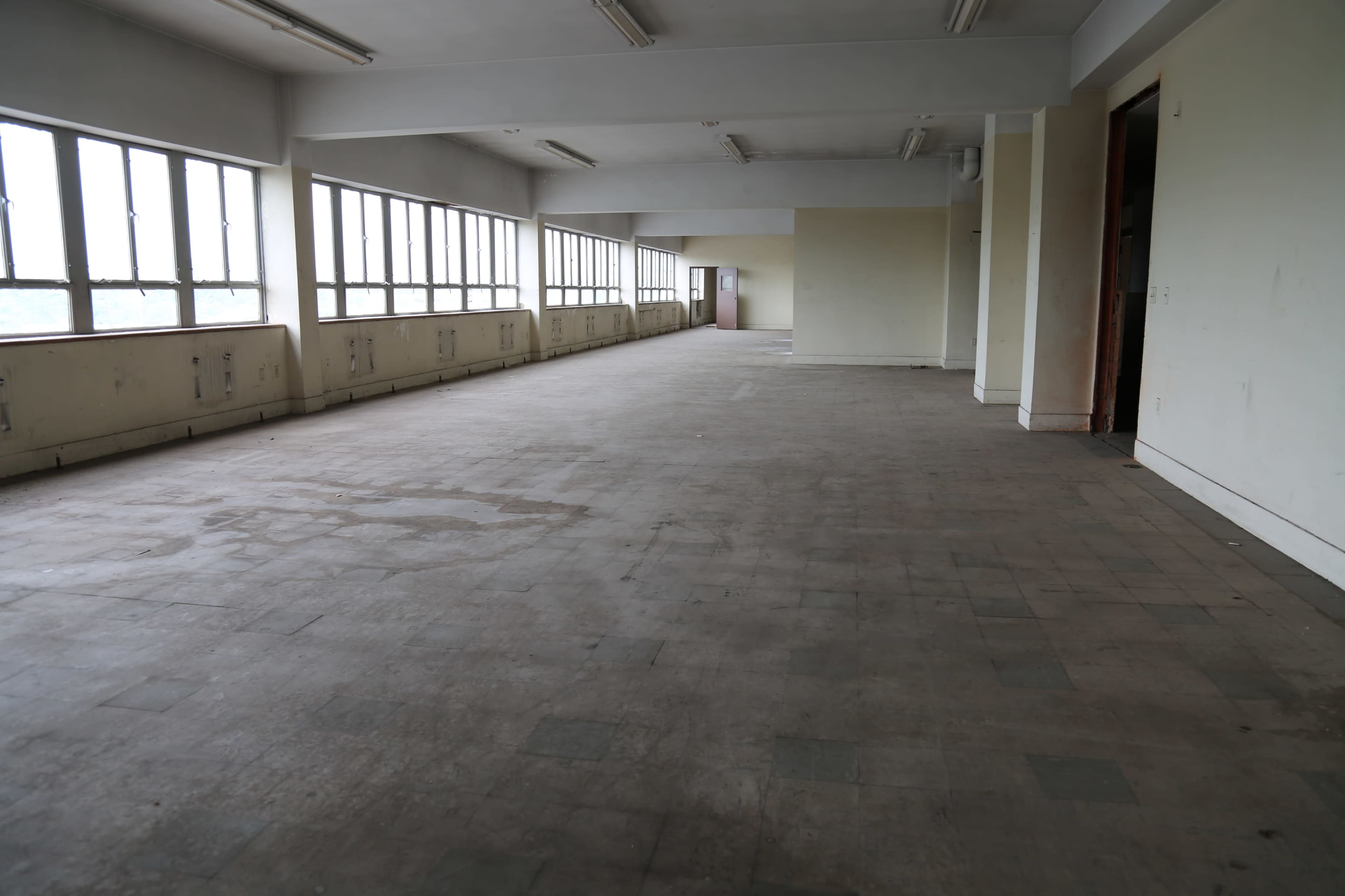 The image shows a spacious, empty room with large windows and a bare floor.