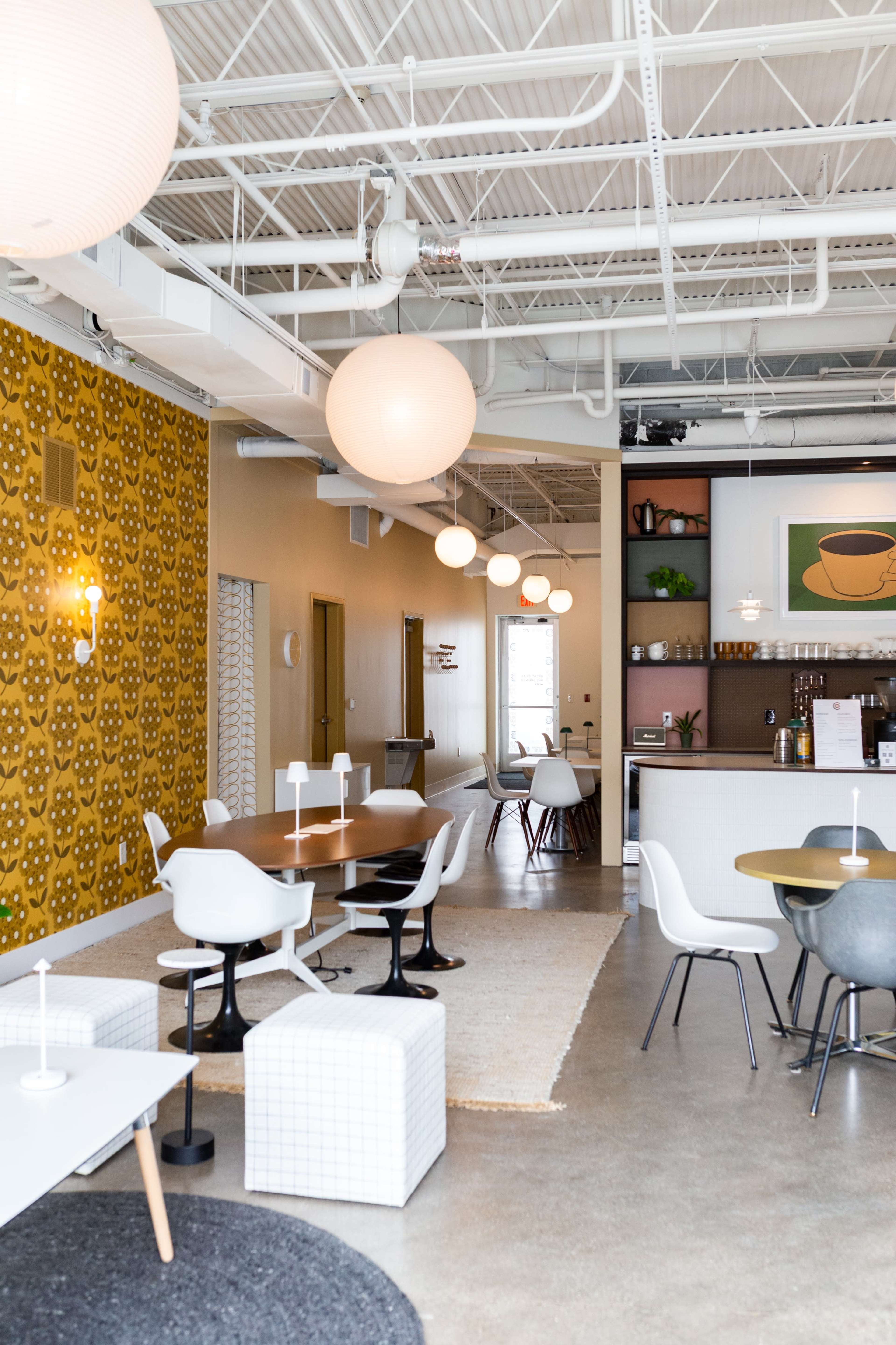 The image shows a modern café interior featuring various seating arrangements, decorative wall patterns, and soft lighting.