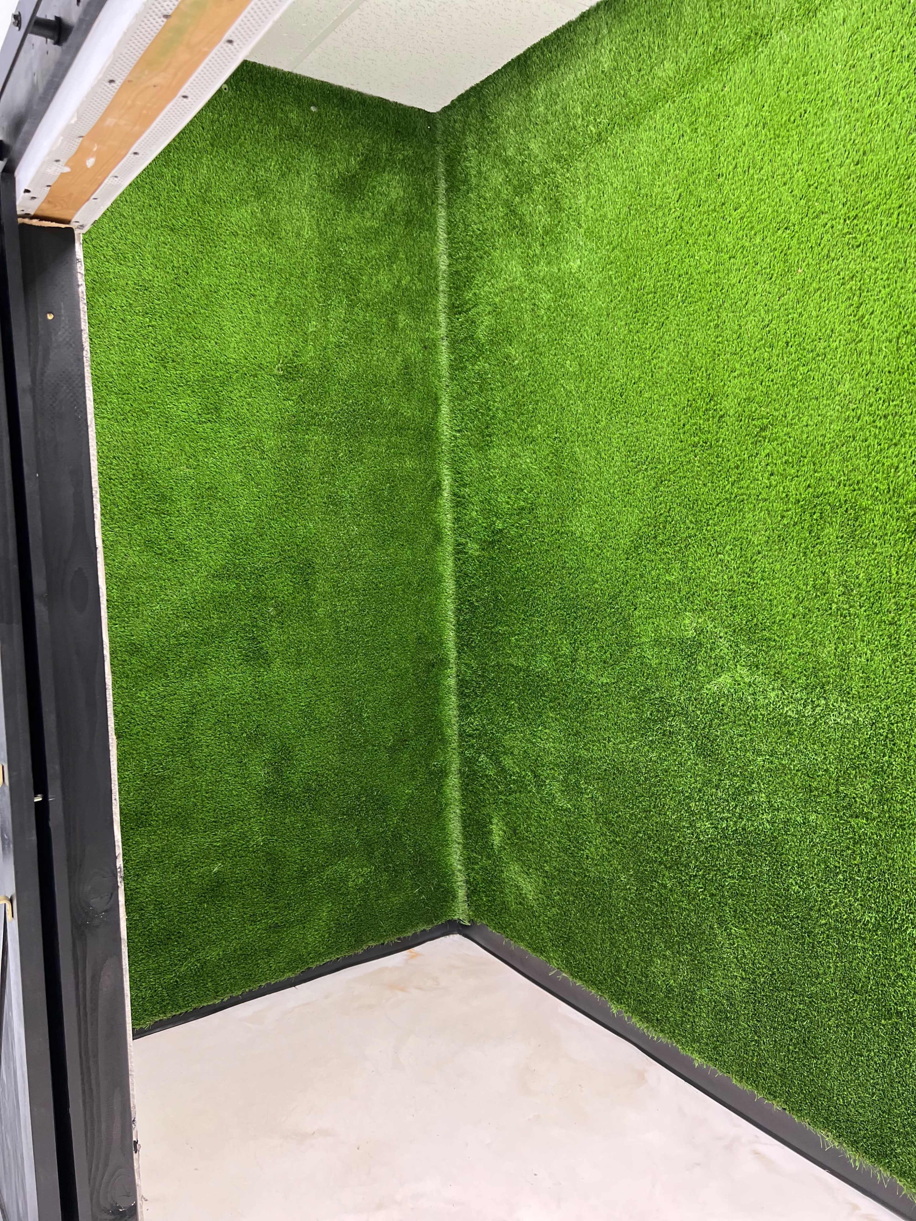 A small room with walls covered in artificial green turf and a bare concrete floor.