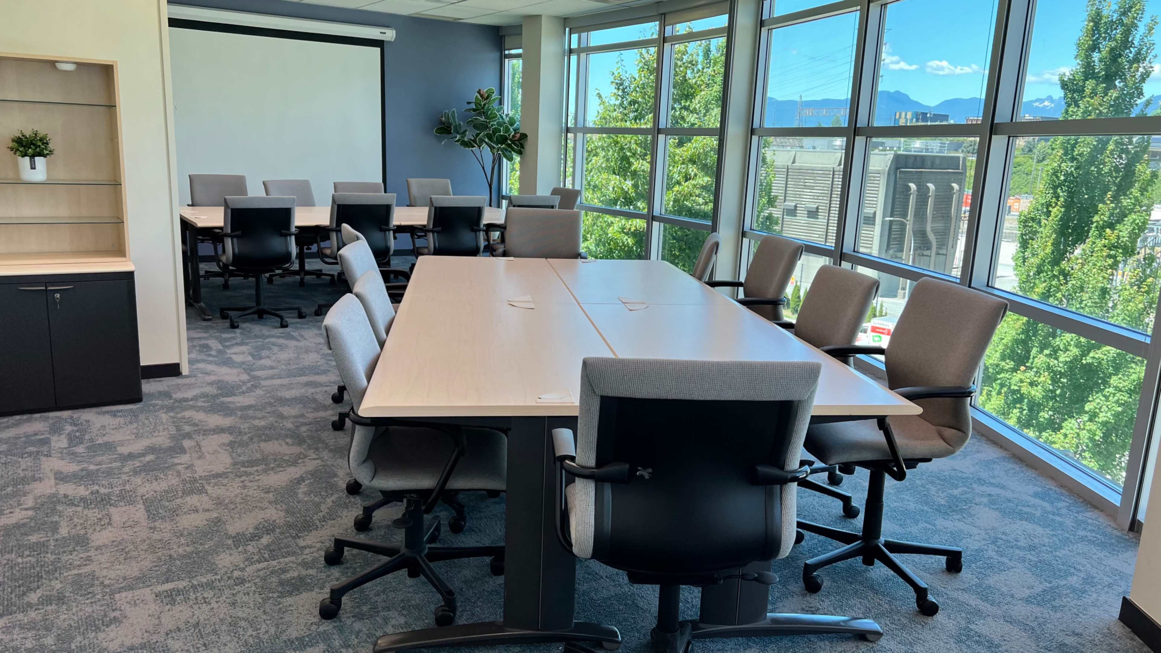 A modern conference room features a large table surrounded by ergonomic chairs, with windows offering a view of the outdoors.