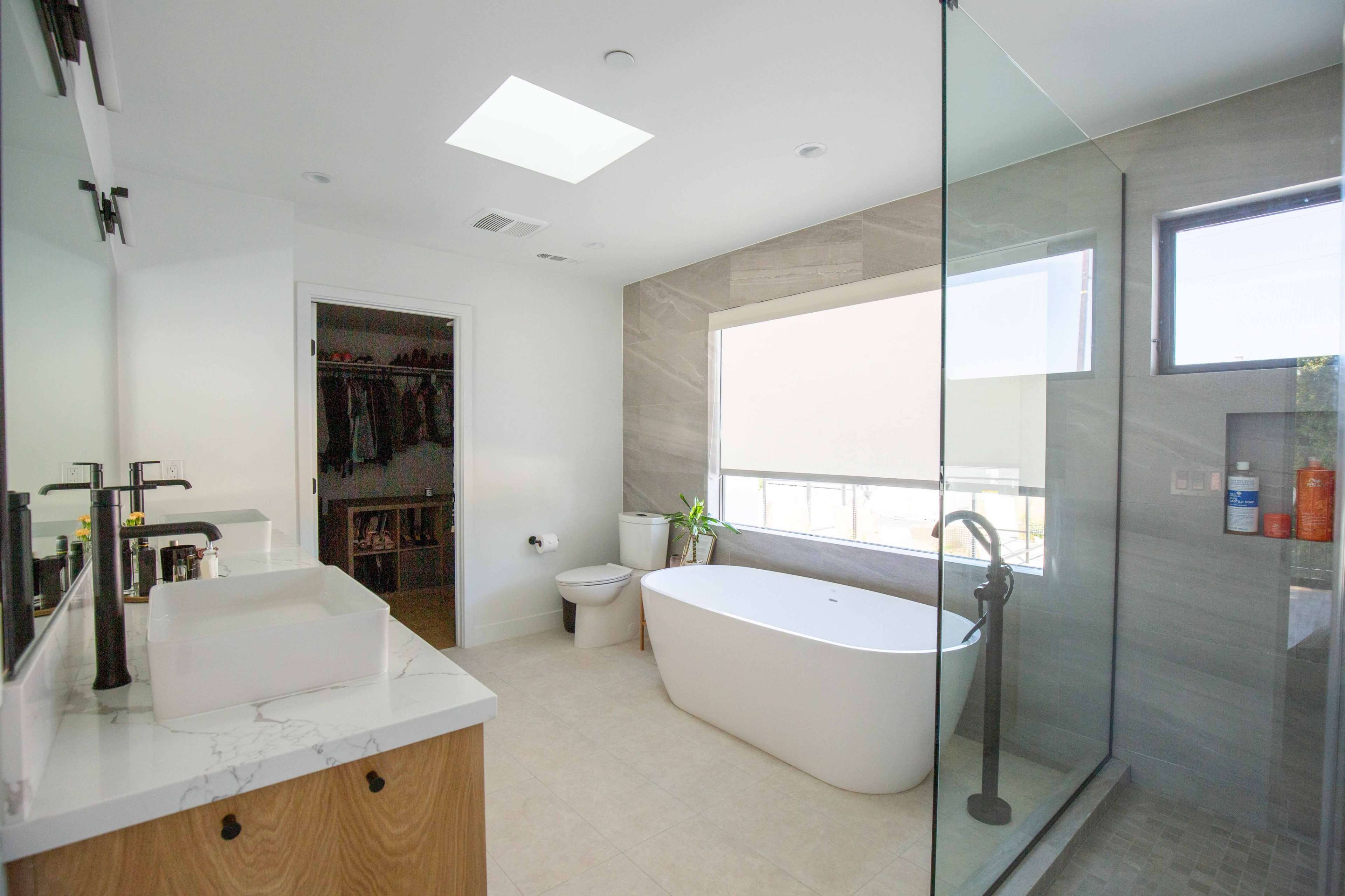 A modern bathroom features a freestanding tub, a walk-in shower with glass walls, and a large window providing natural light.
