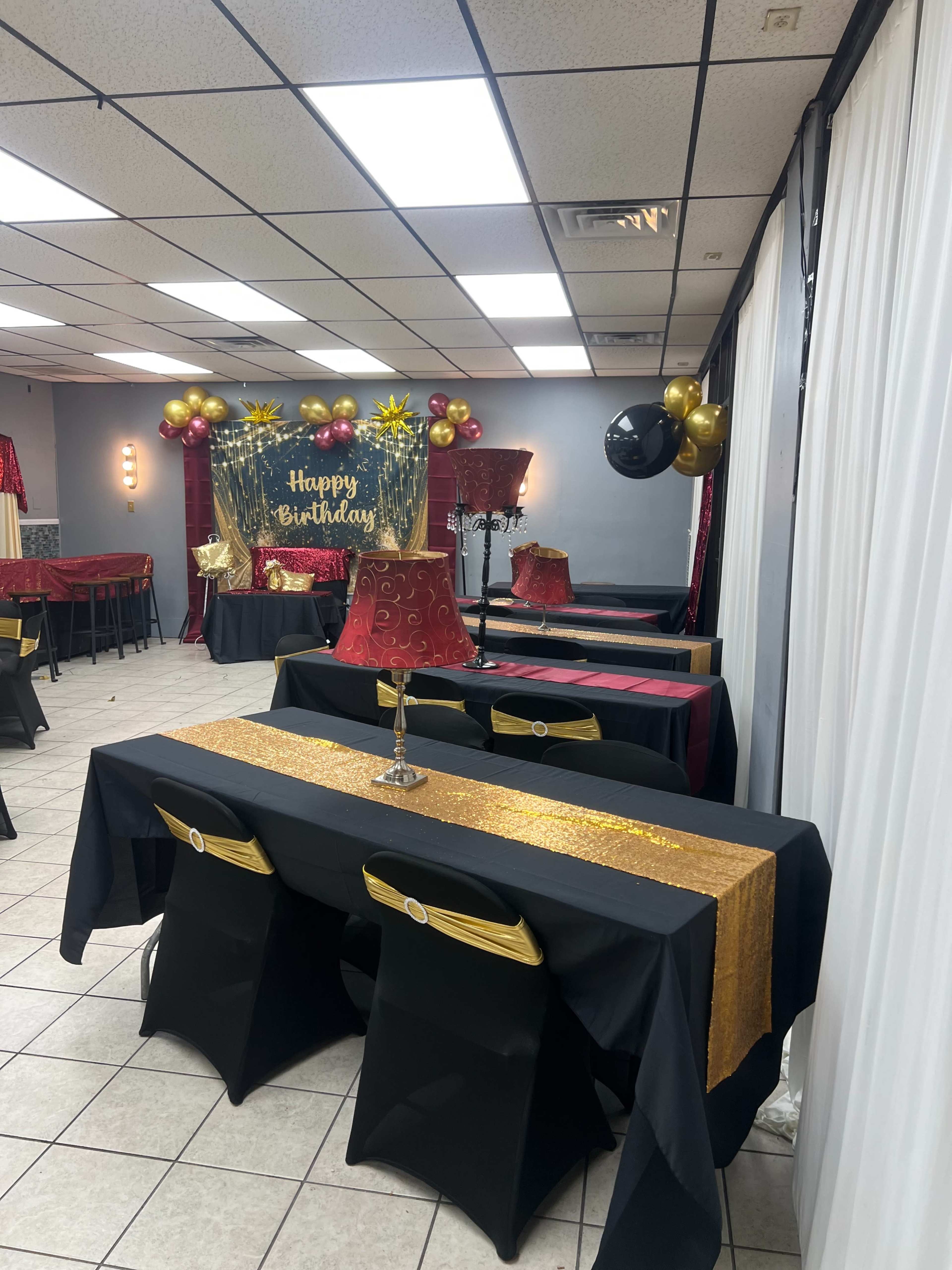 The image shows a birthday party setup with decorated tables featuring black and gold table runners, along with balloons and a "Happy Birthday" banner in the background.