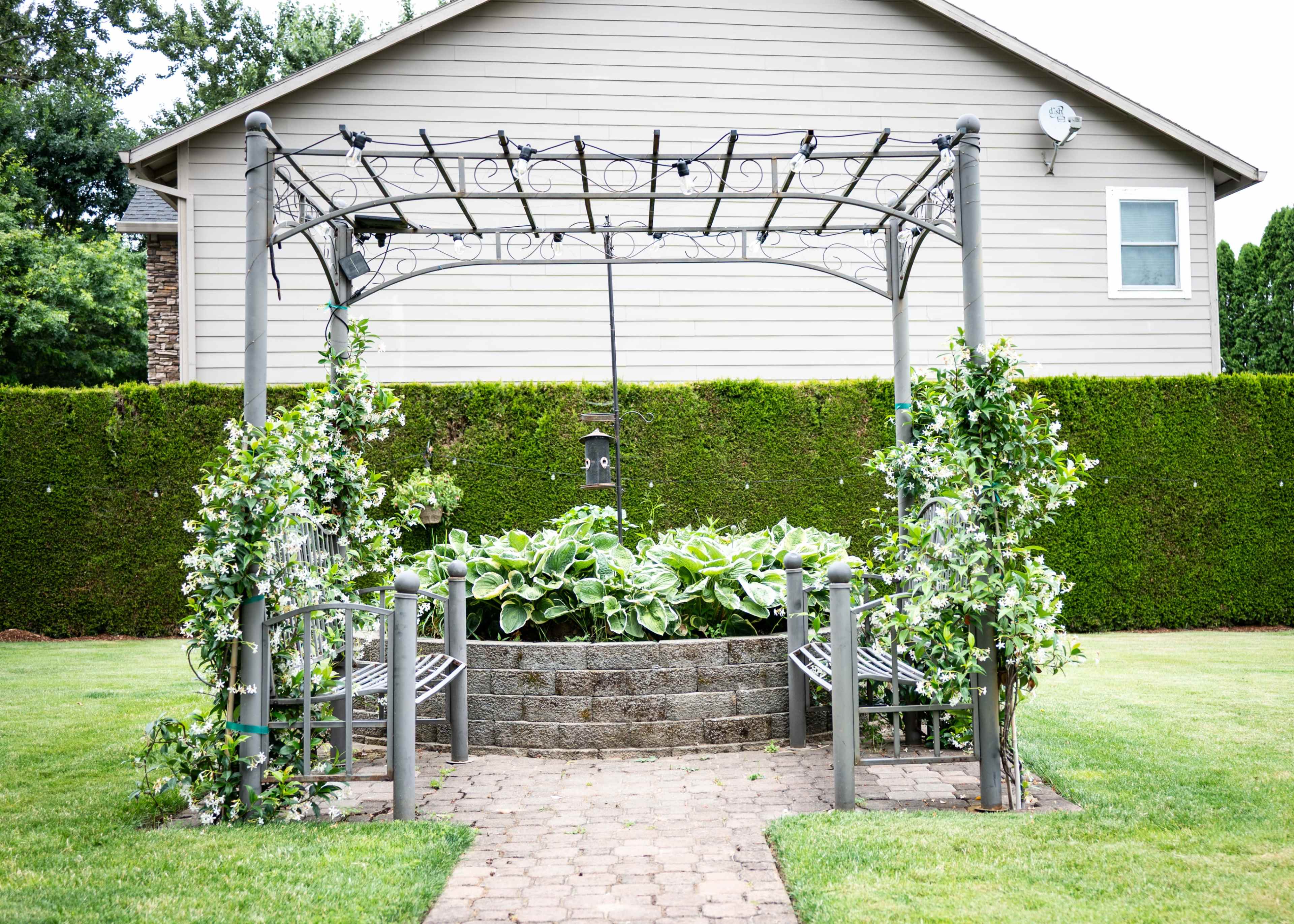 The image shows a garden structure with a decorative archway surrounded by benches and lush greenery.