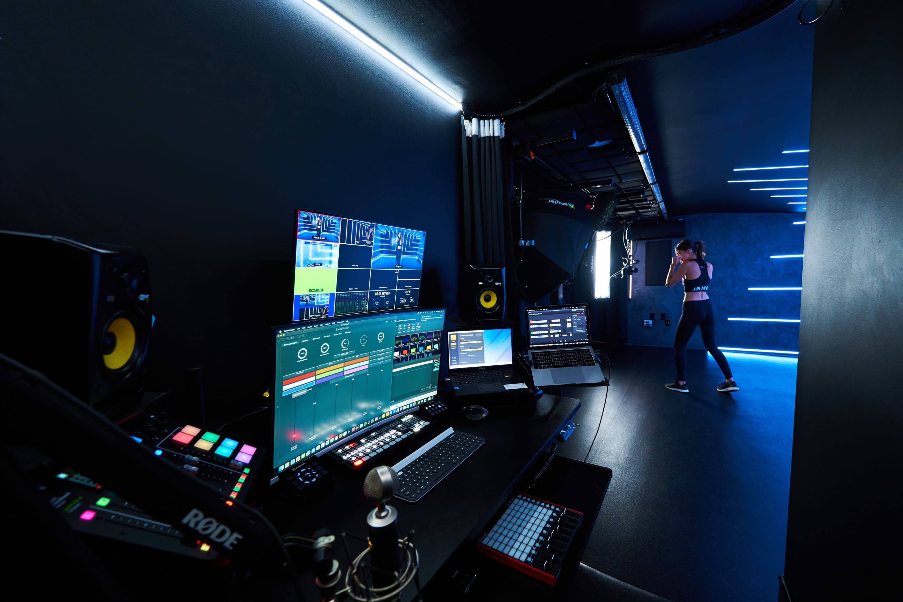 A modern studio setup features multiple screens and audio equipment, while a person is standing in a performance area.