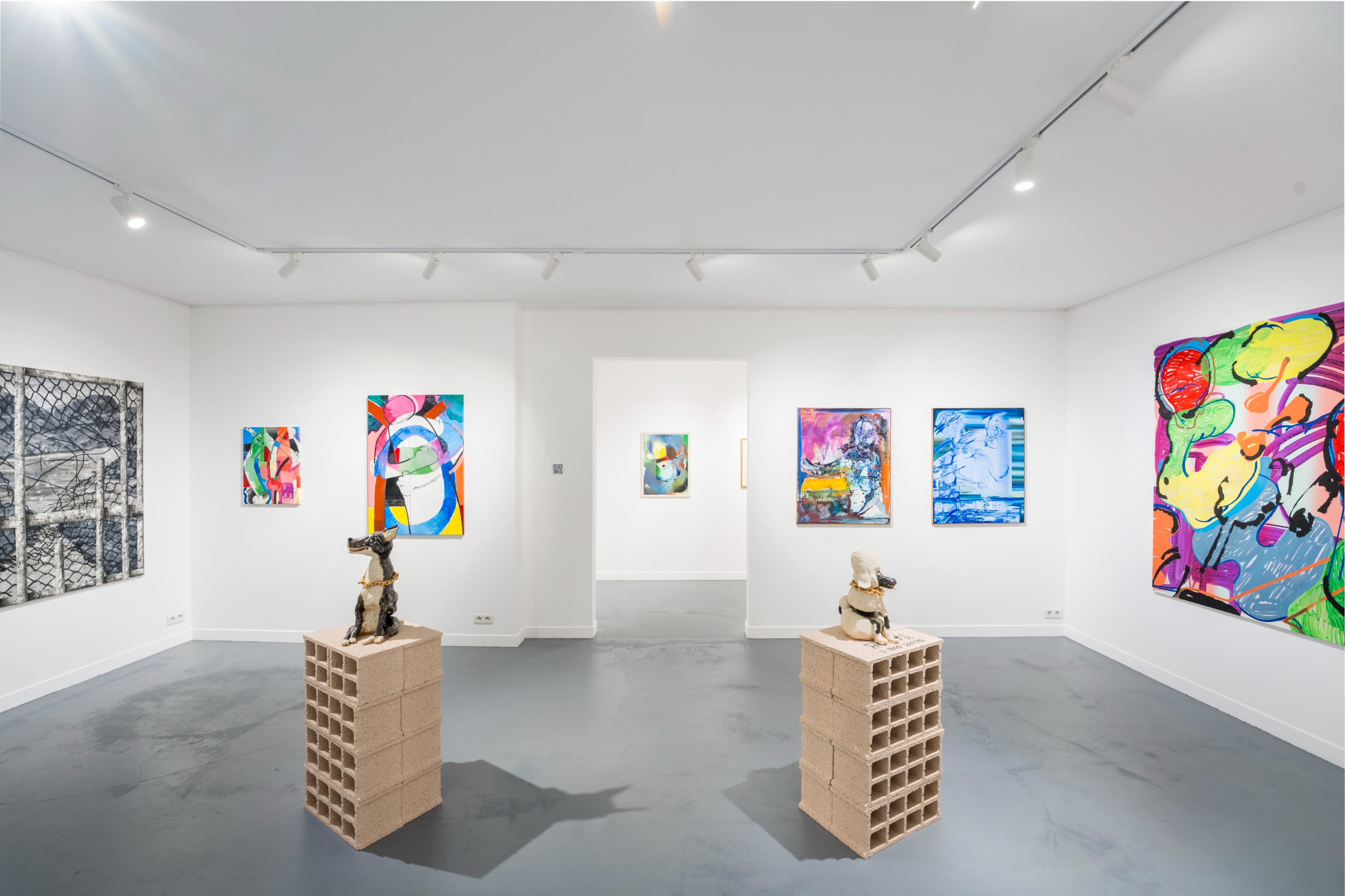 The image shows an art gallery featuring colorful paintings on the walls and two sculptures displayed on pedestal-like structures made of bricks in the center.