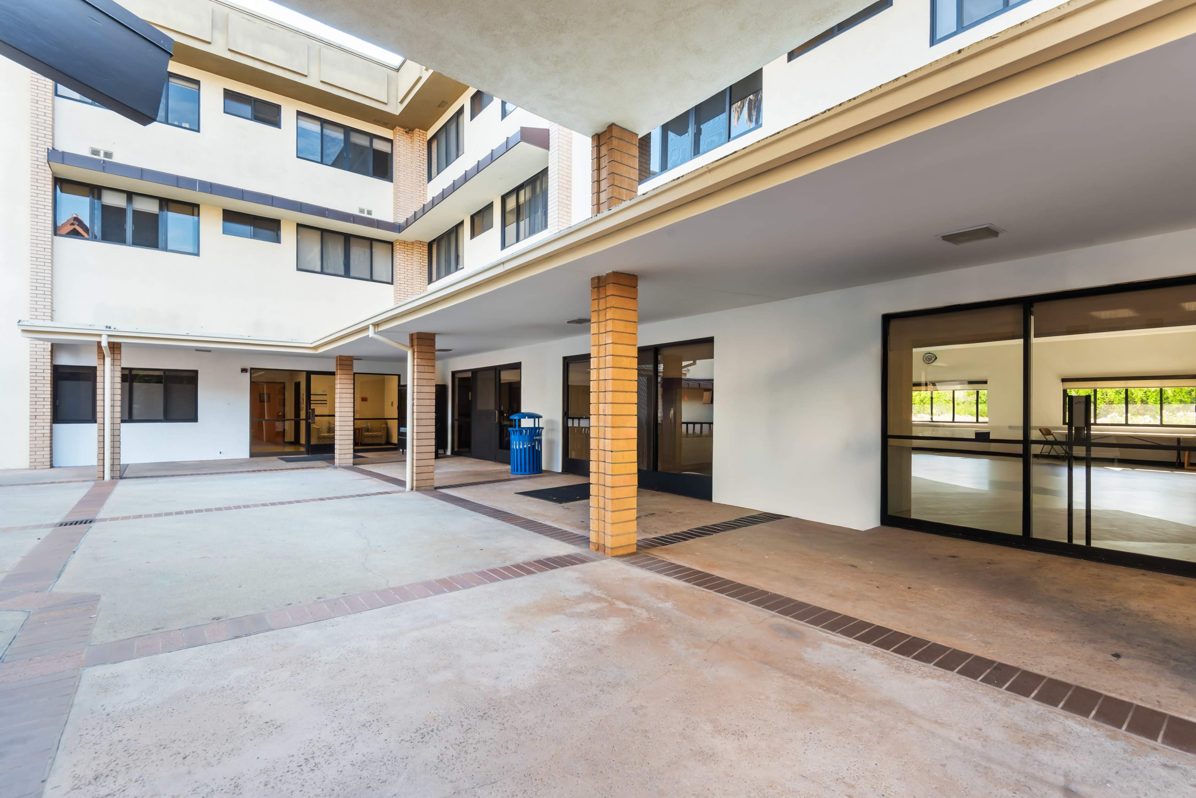 The image shows a multi-story building with a covered walkway and large glass windows, revealing an empty interior space.