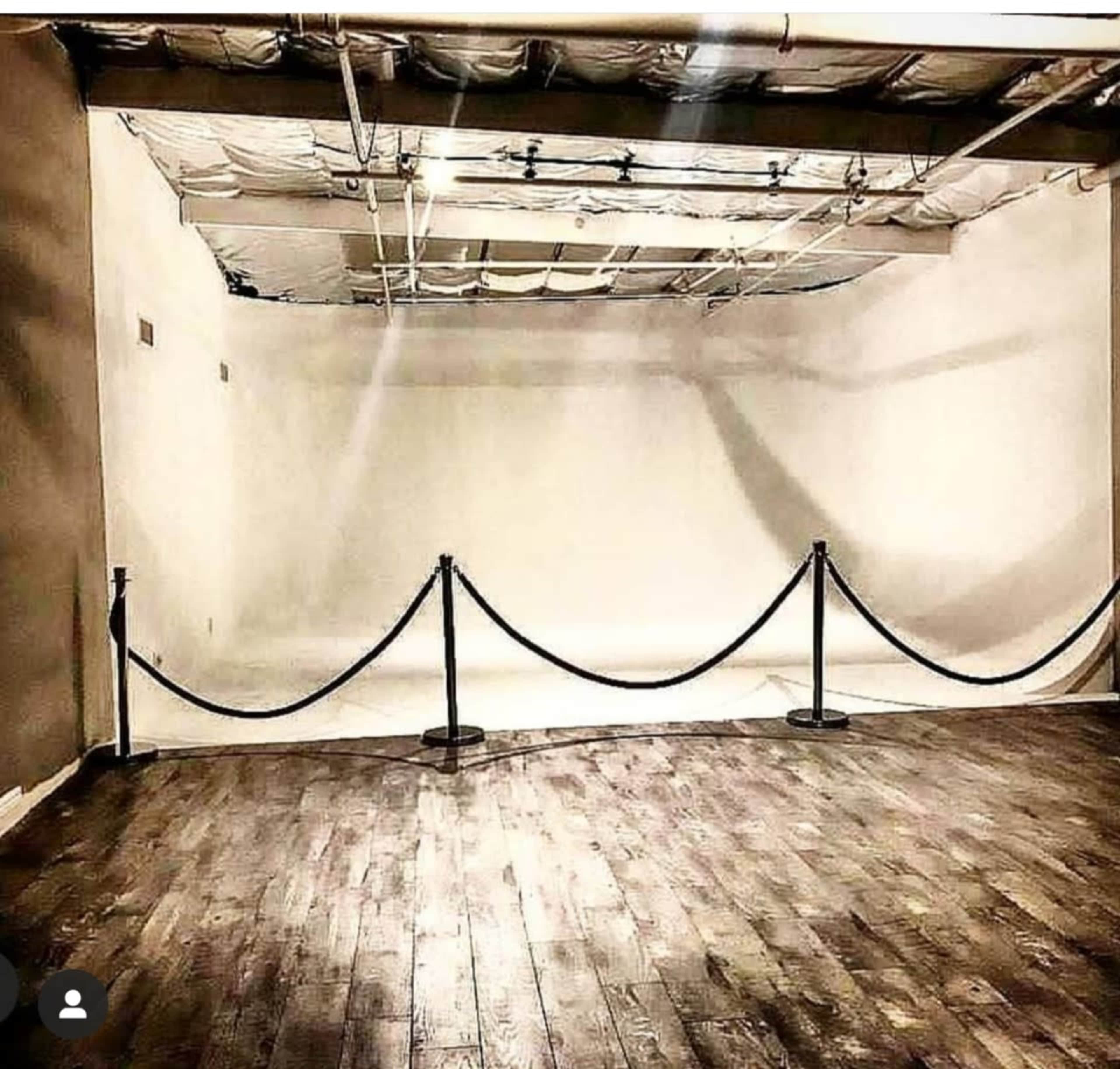 An empty, well-lit studio room with a wooden floor and a rope barrier along one side.