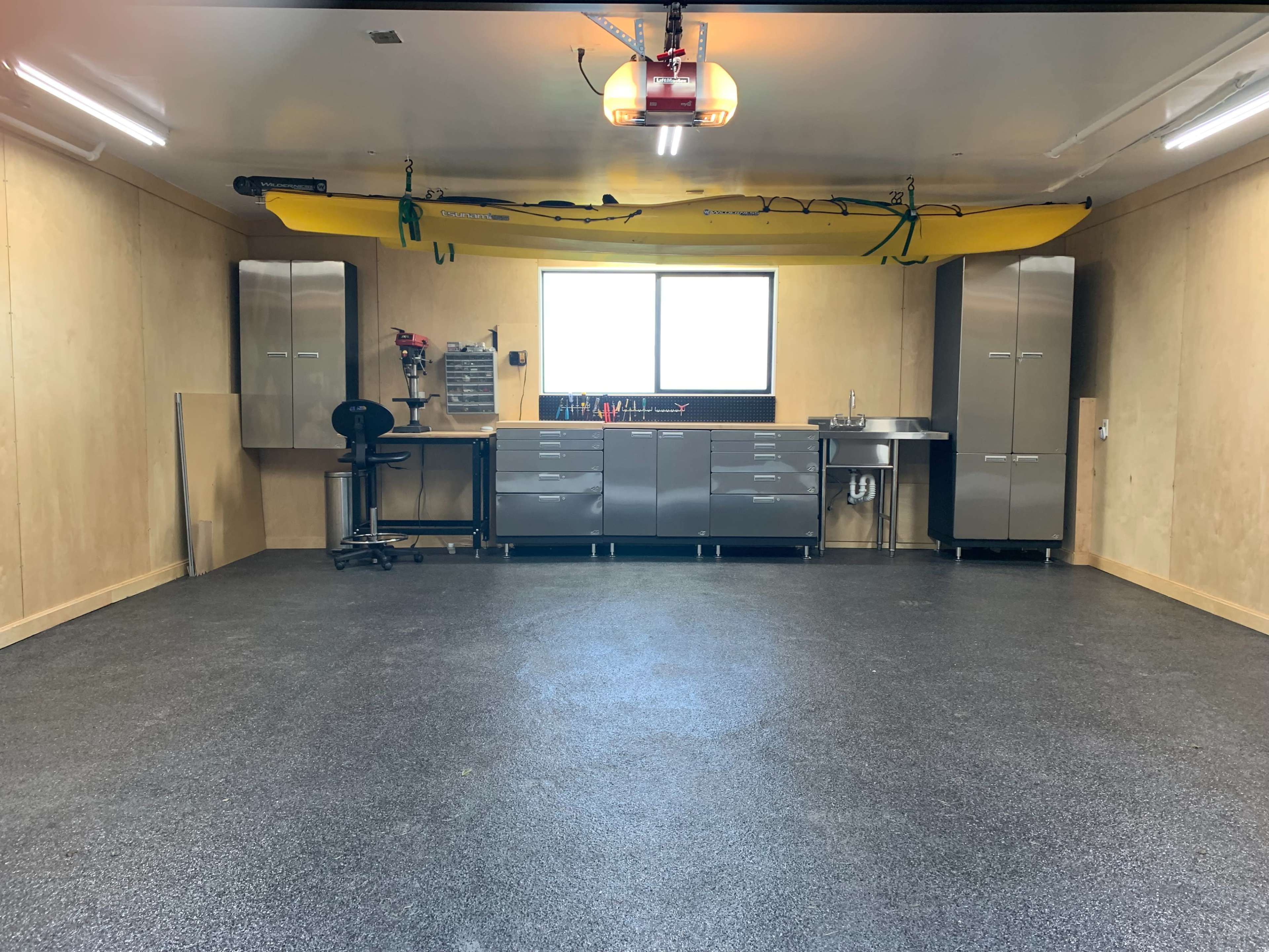 A spacious garage with gray walls, a yellow kayak suspended from the ceiling, and metal cabinets along the back wall.