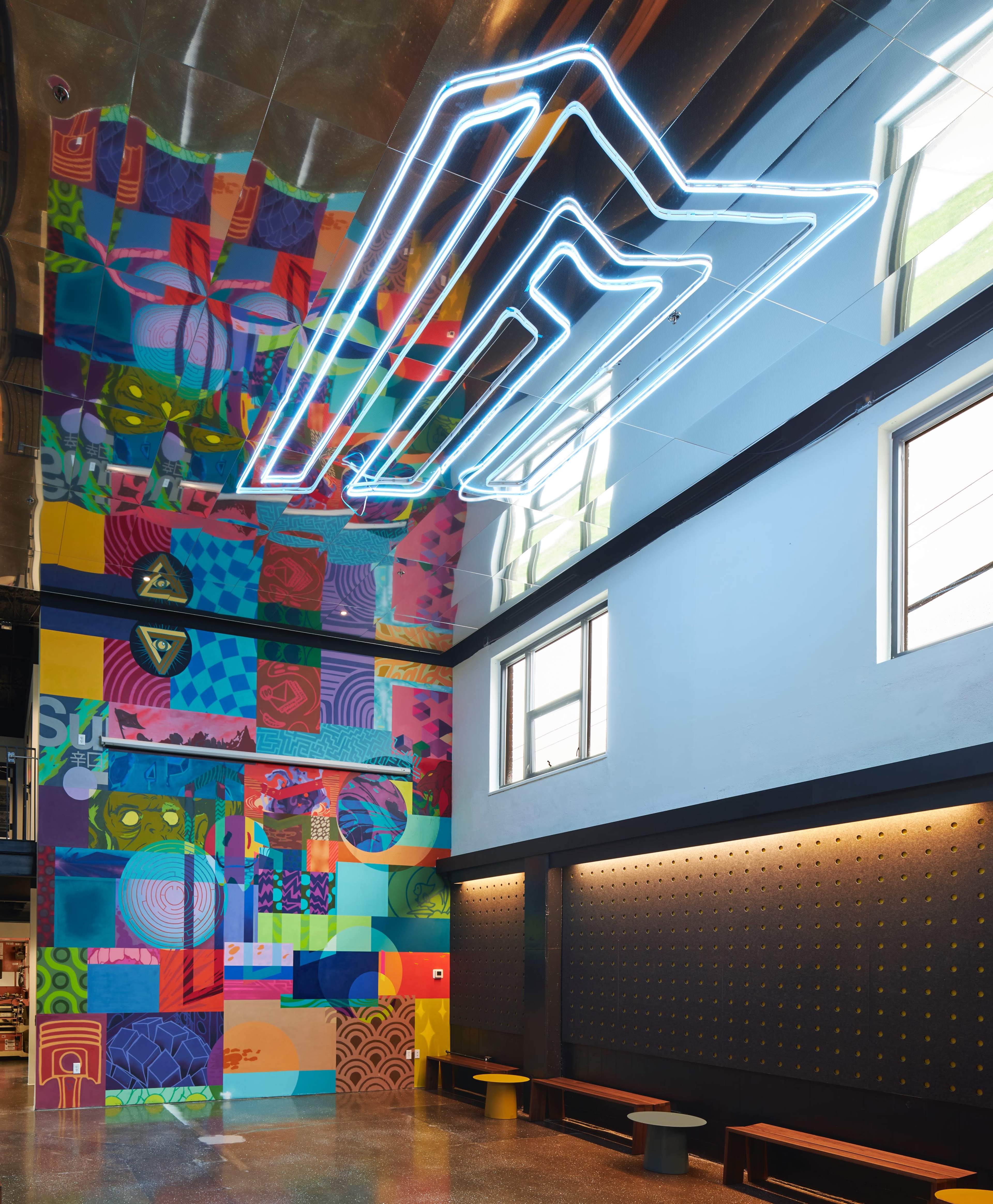 A modern interior space with a colorful mural on one wall and a neon sign on the ceiling.