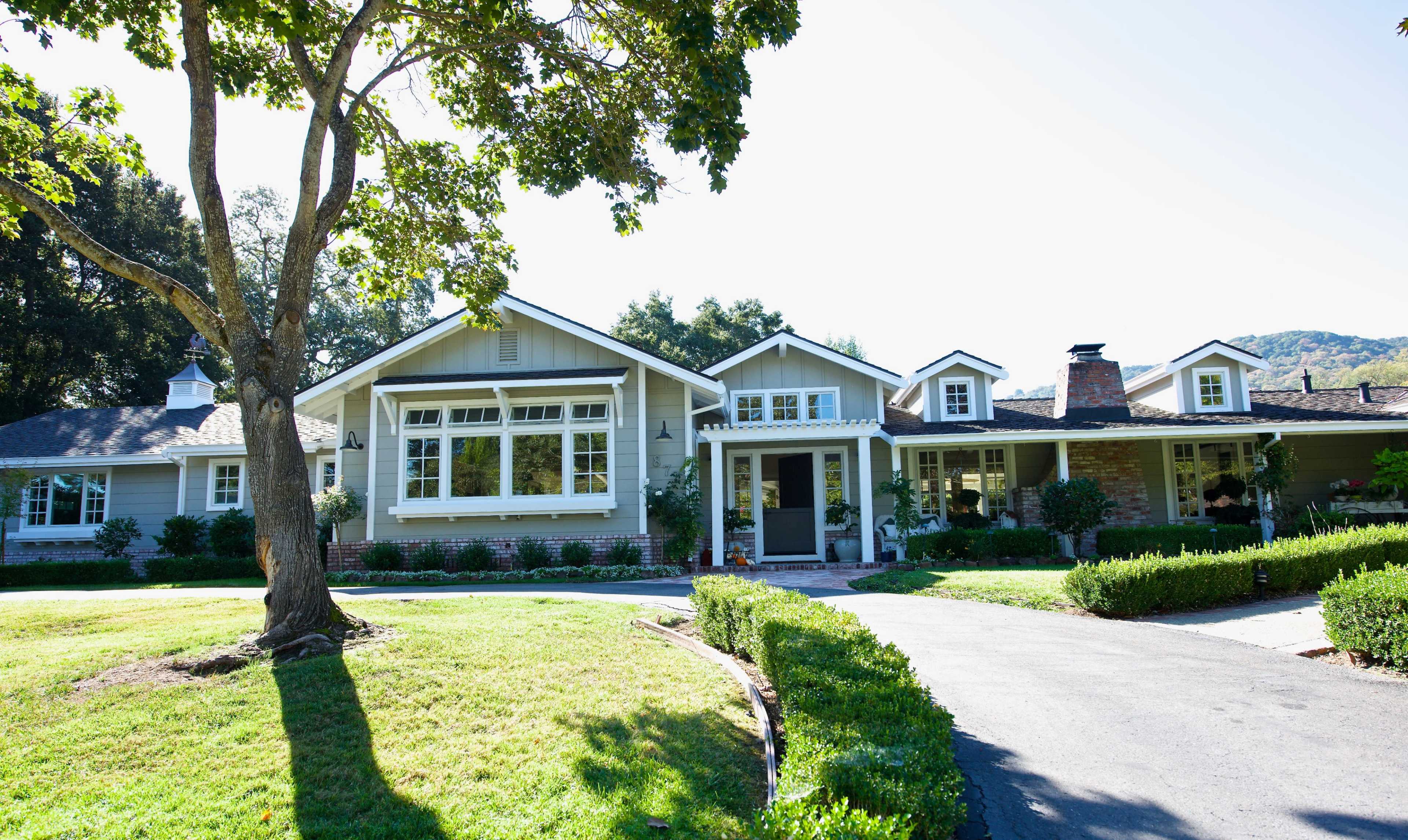 A large, light-colored house with multiple gables and a well-maintained lawn, surrounded by trees and shrubs.