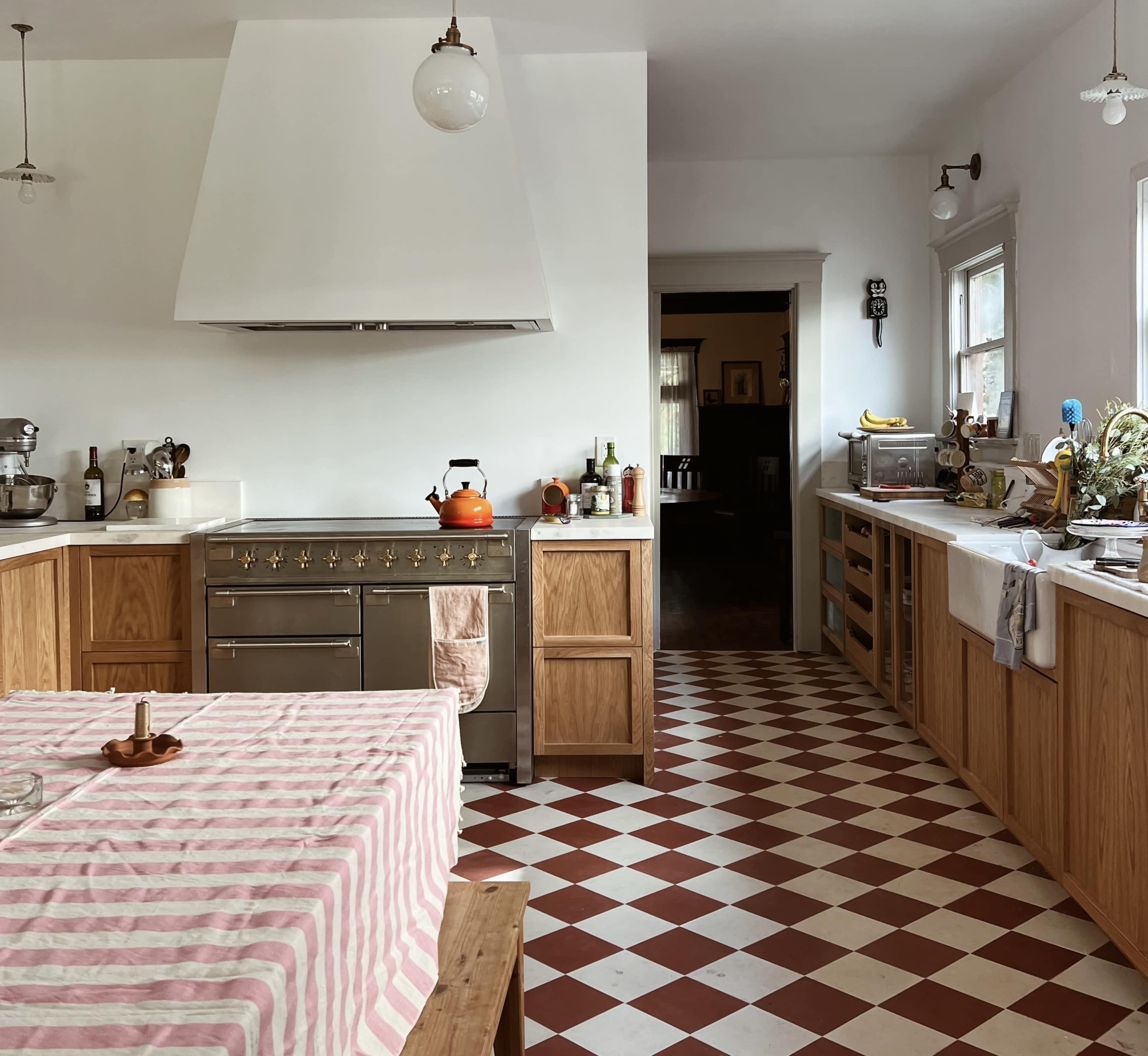 A kitchen features a striped tablecloth, a large stove with a hood, and wooden cabinets with a checkered floor.