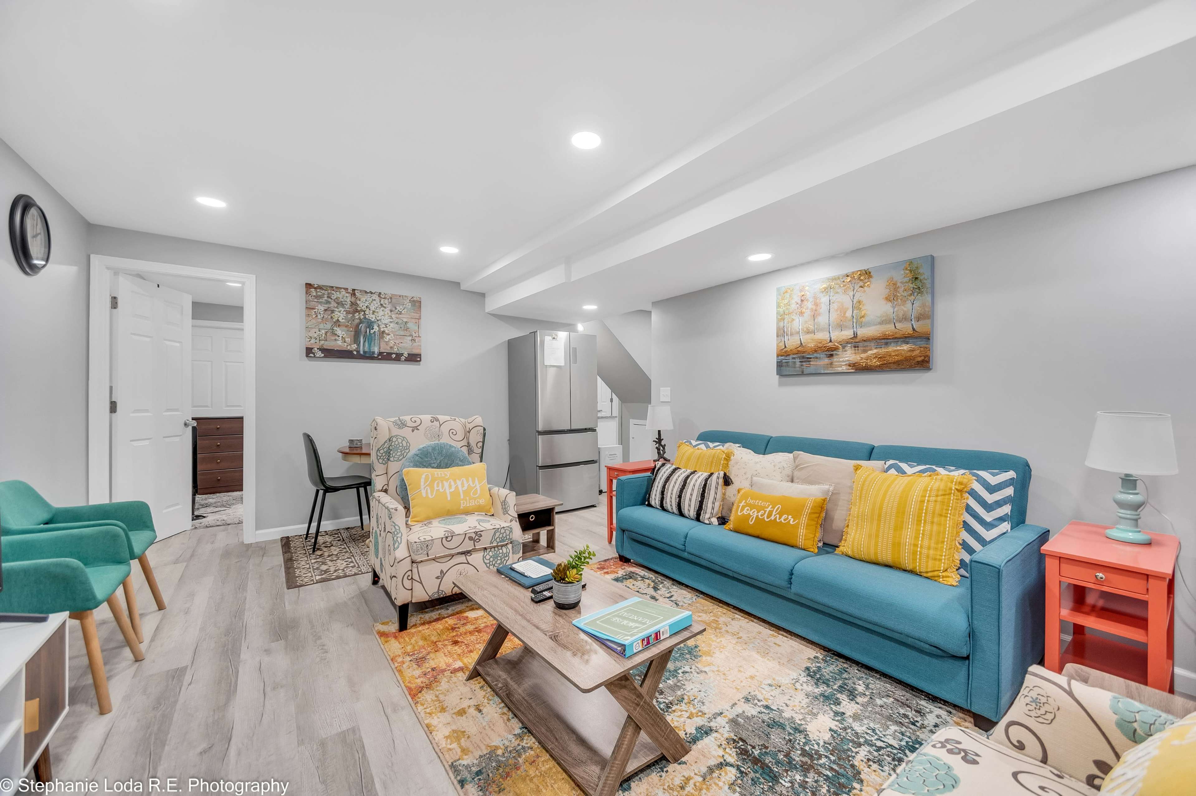 A modern, well-lit basement living area with a blue sofa, decorative chairs, and a coffee table set on a light wooden floor.