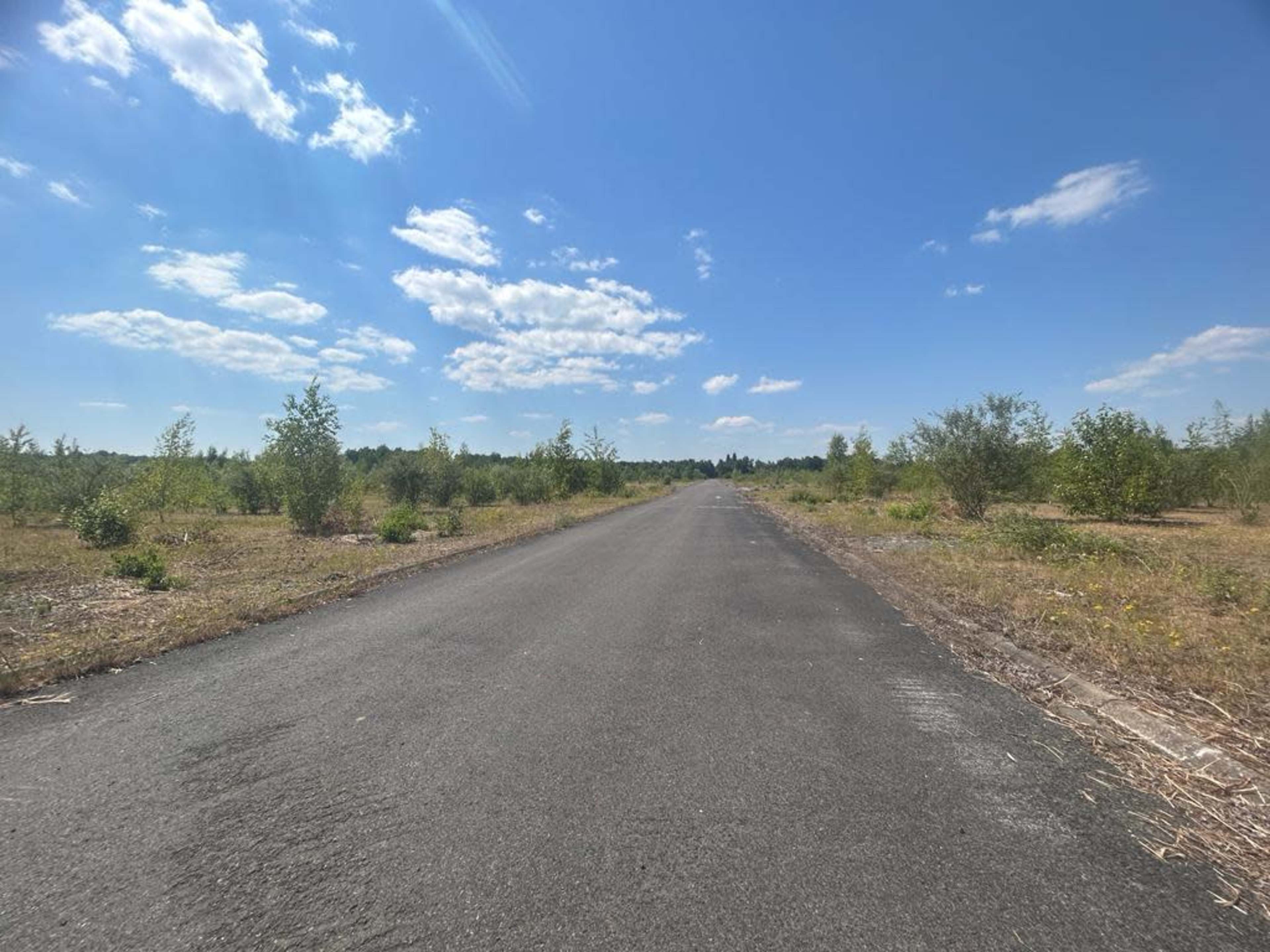 A straight, empty road stretches through a sparsely vegetated landscape under a partly cloudy sky.