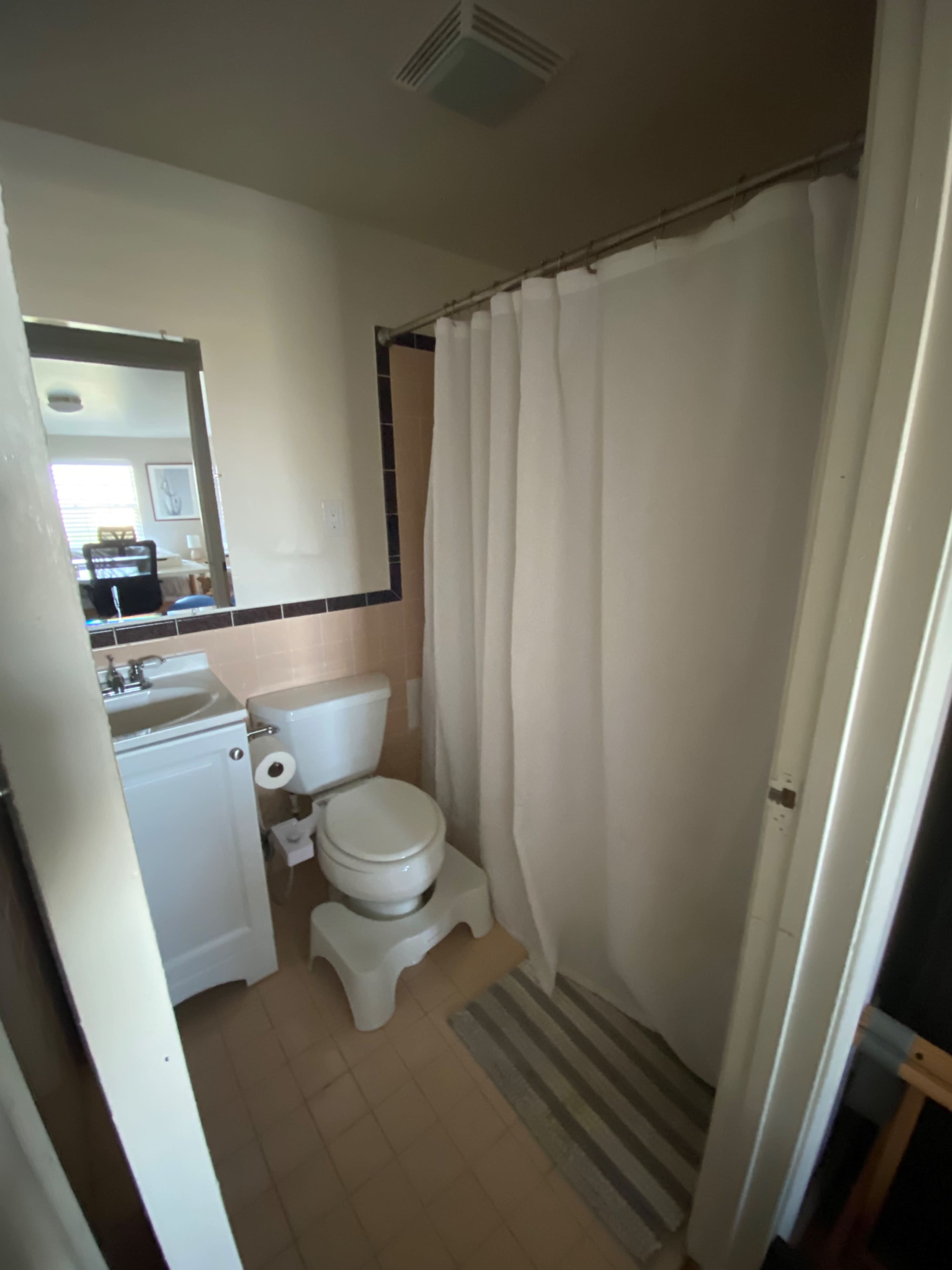 A small bathroom with a shower curtain, toilet, sink, and a striped rug on the floor.