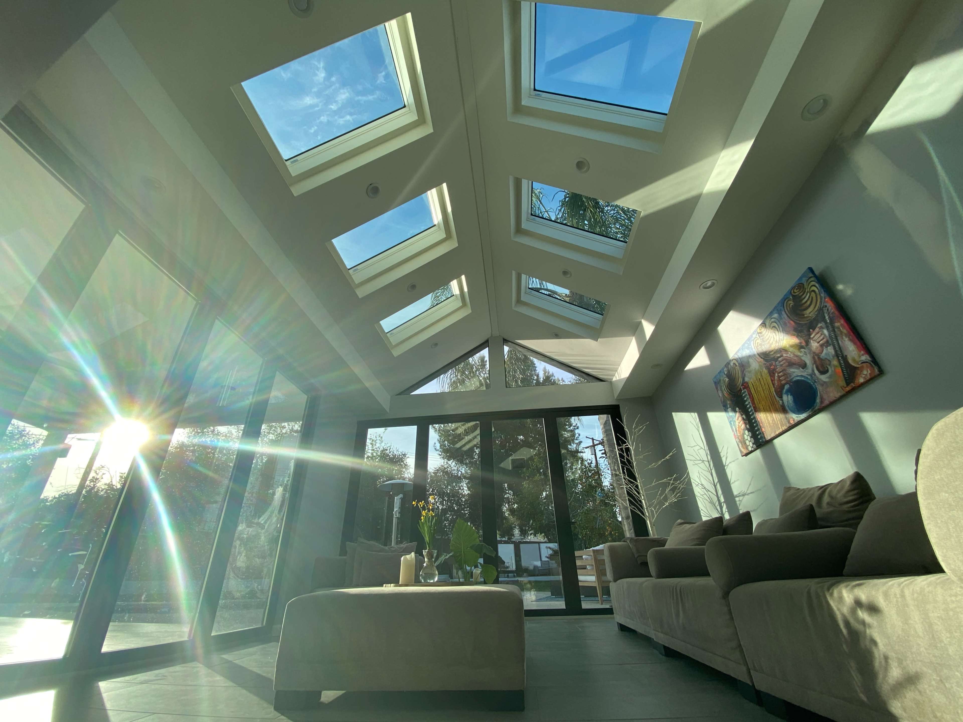 A modern living room with large skylights and glass doors, allowing natural light to flood the space while offering a view of the outdoors.
