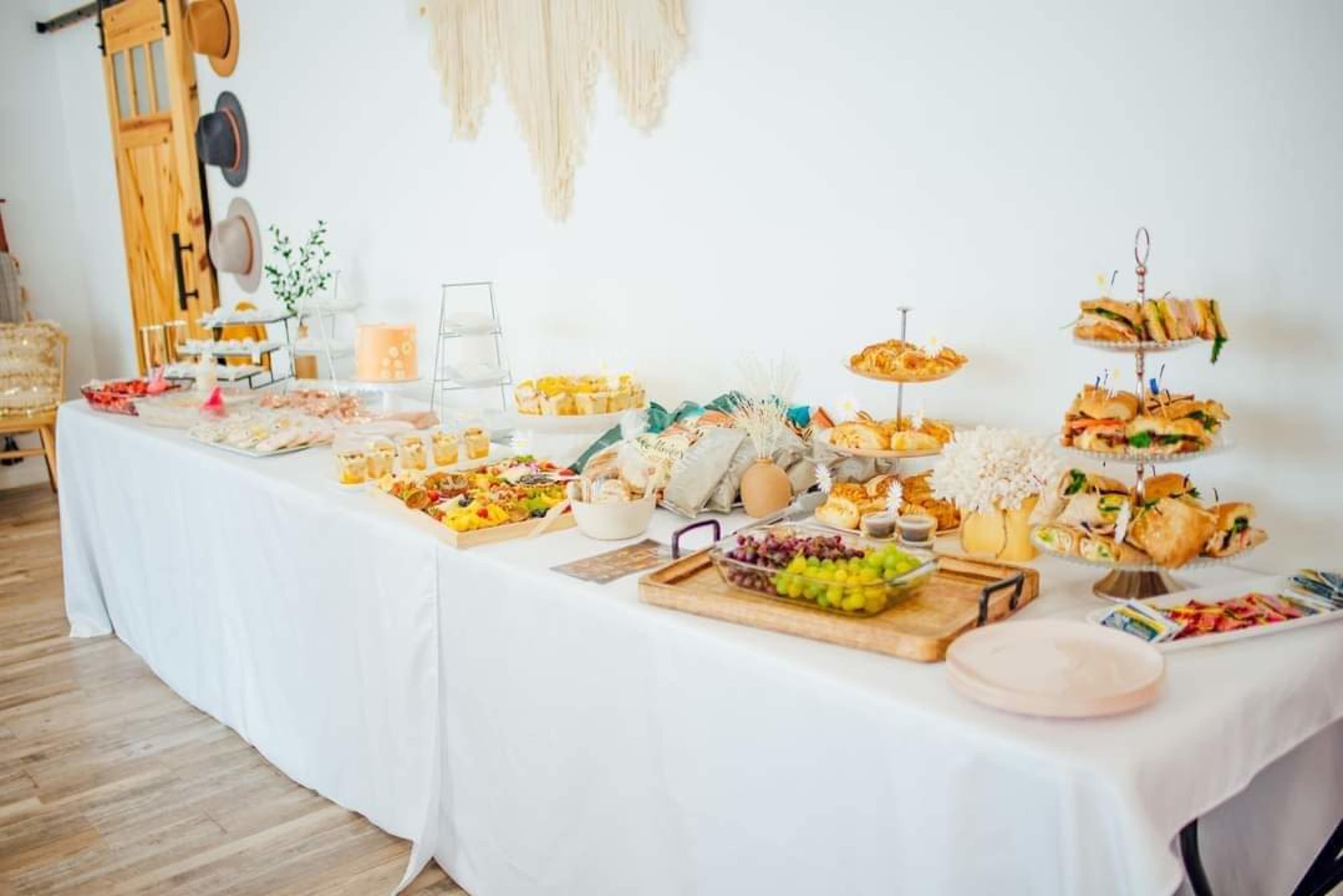 A long table is set with an assortment of food, including sandwiches, desserts, fruit, and decorative items.
