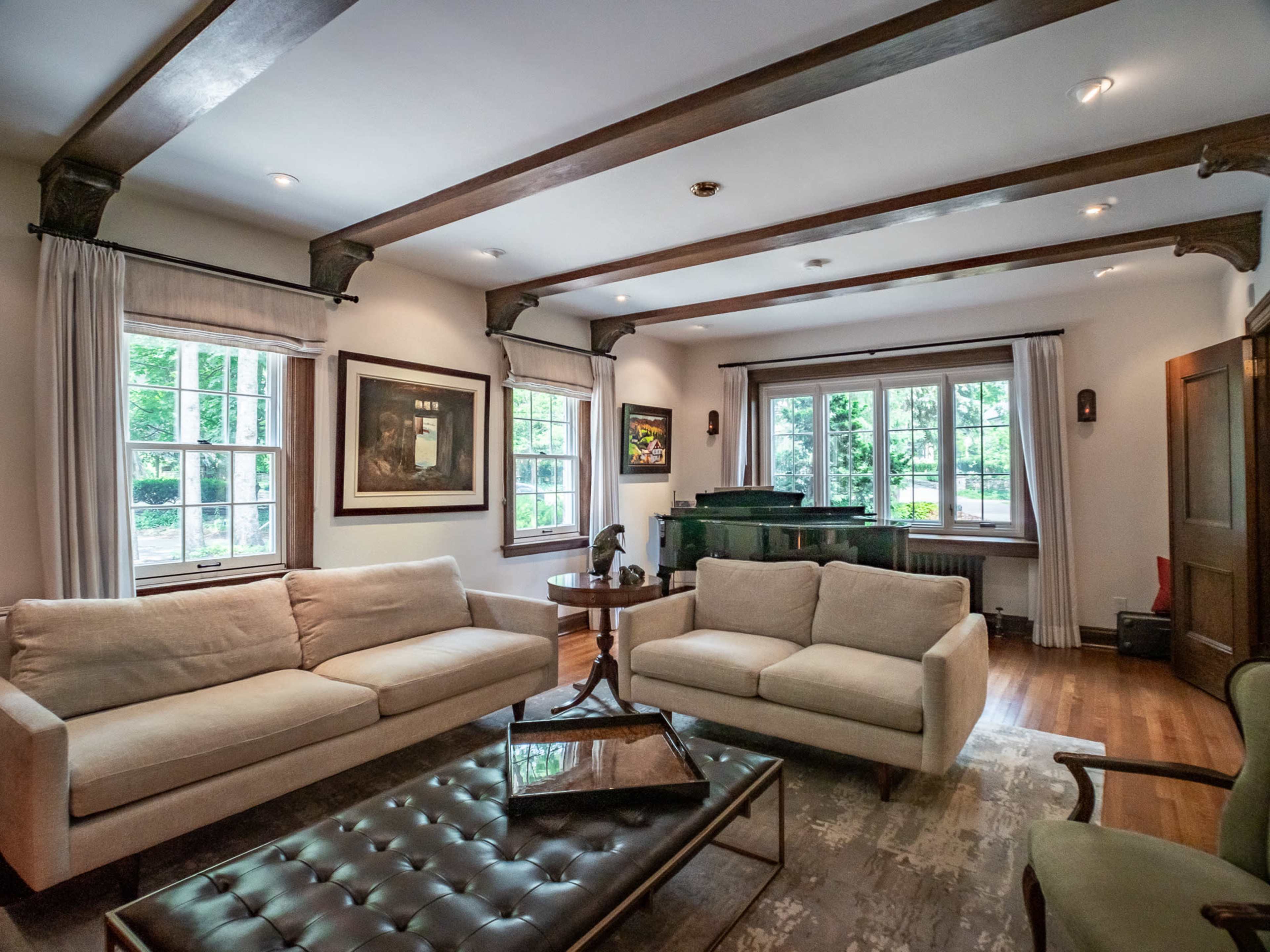 A living room with two sofas, a glass coffee table, and a piano near large windows that provide natural light.