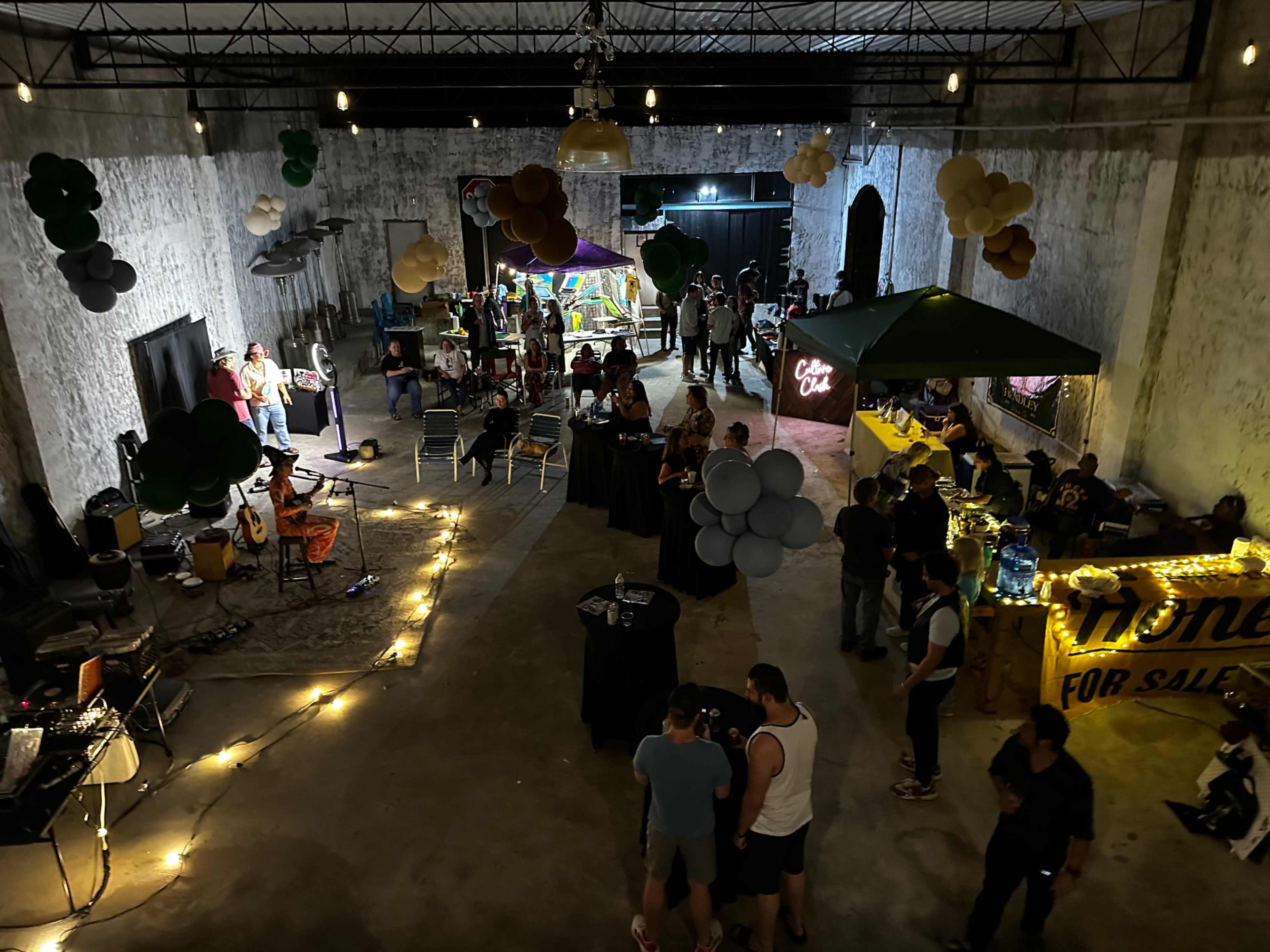 A large indoor space is filled with people socializing, eating, and enjoying entertainment amidst decorative balloons and ambient lighting.