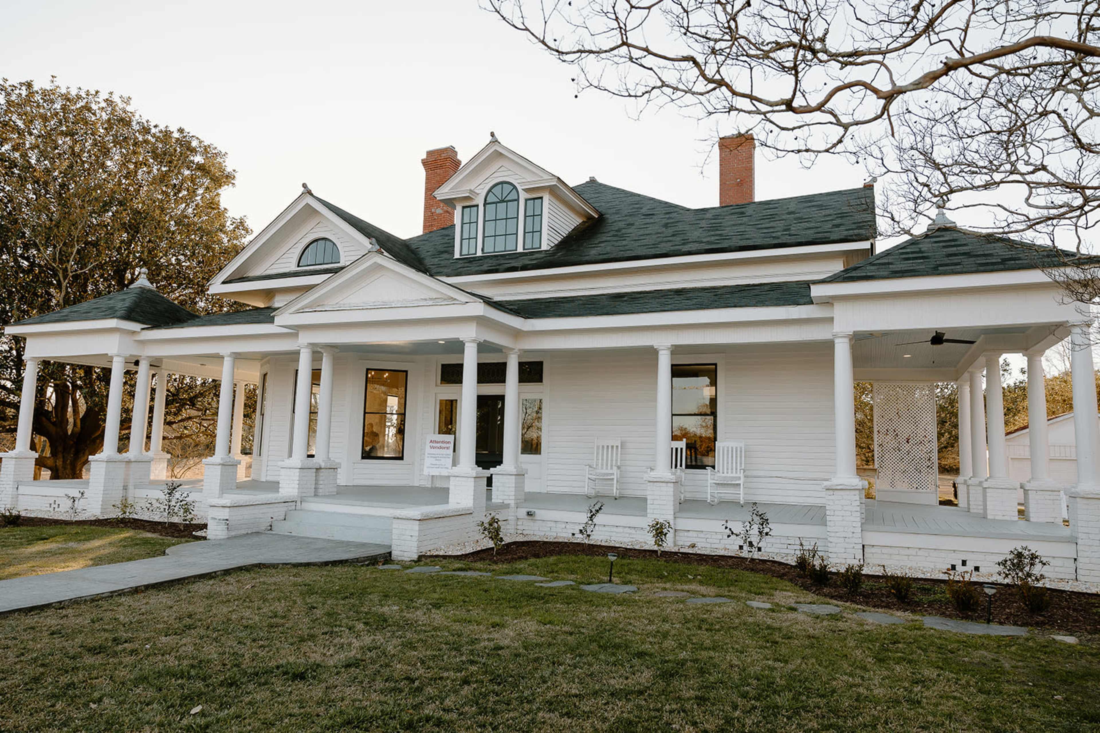 A large, white two-story house with a wraparound porch, multiple gabled roofs, and a well-manicured lawn.