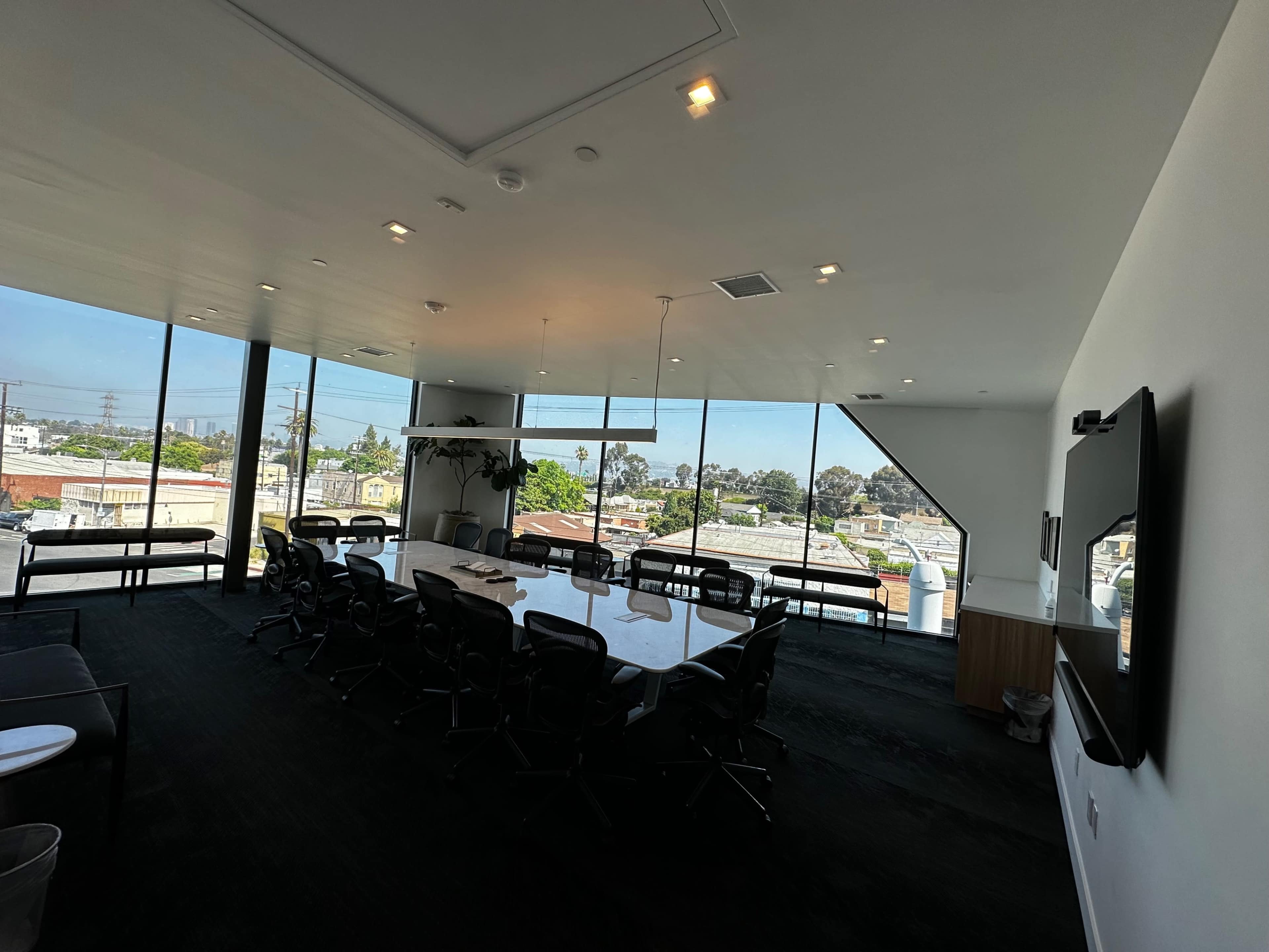 The image shows a modern conference room with a large table surrounded by chairs and large windows offering a view of the surrounding area.
