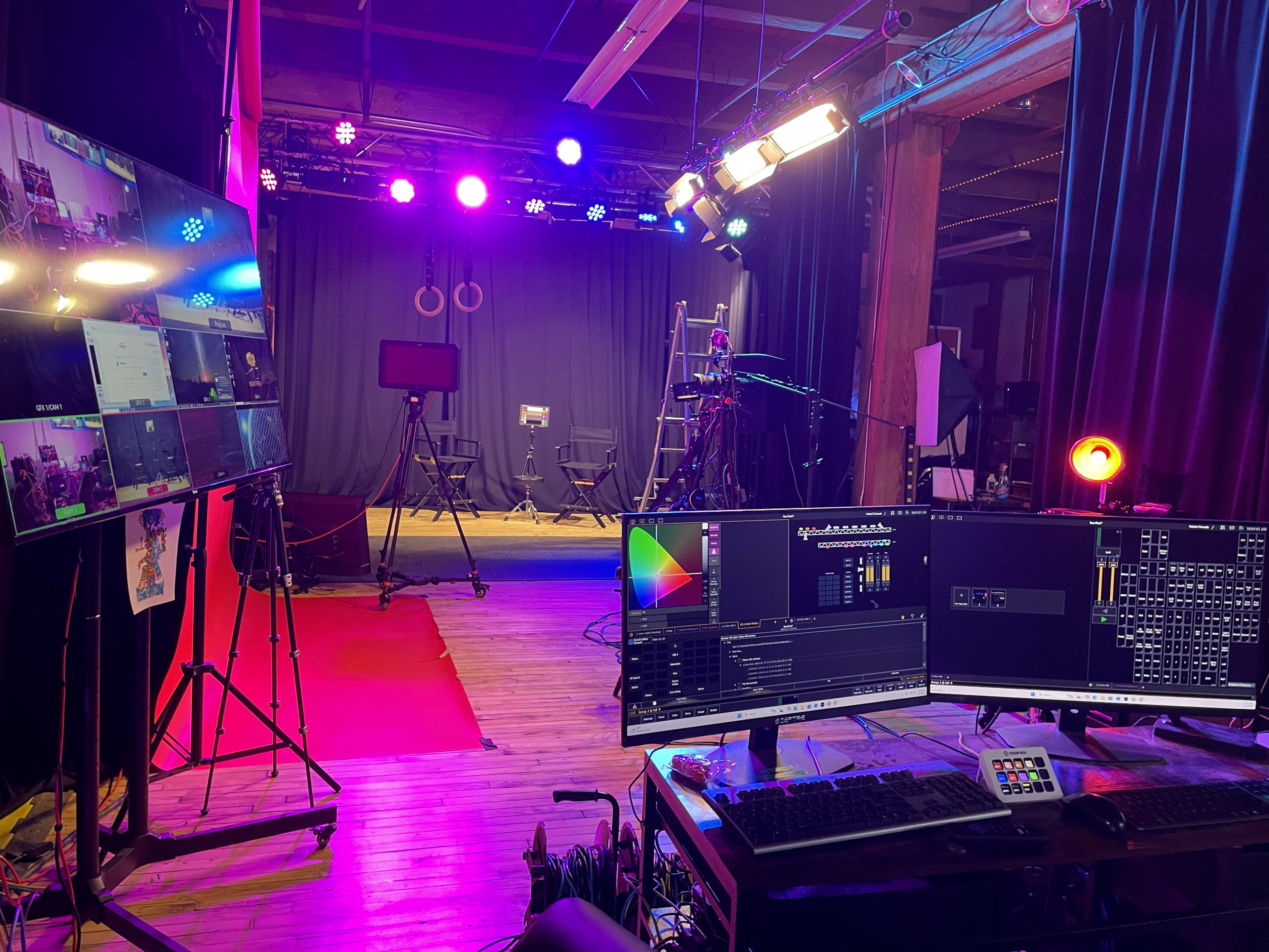 The image shows a studio setup with multiple screens displaying live feeds, lighting equipment, and chairs arranged in front of a dark backdrop.