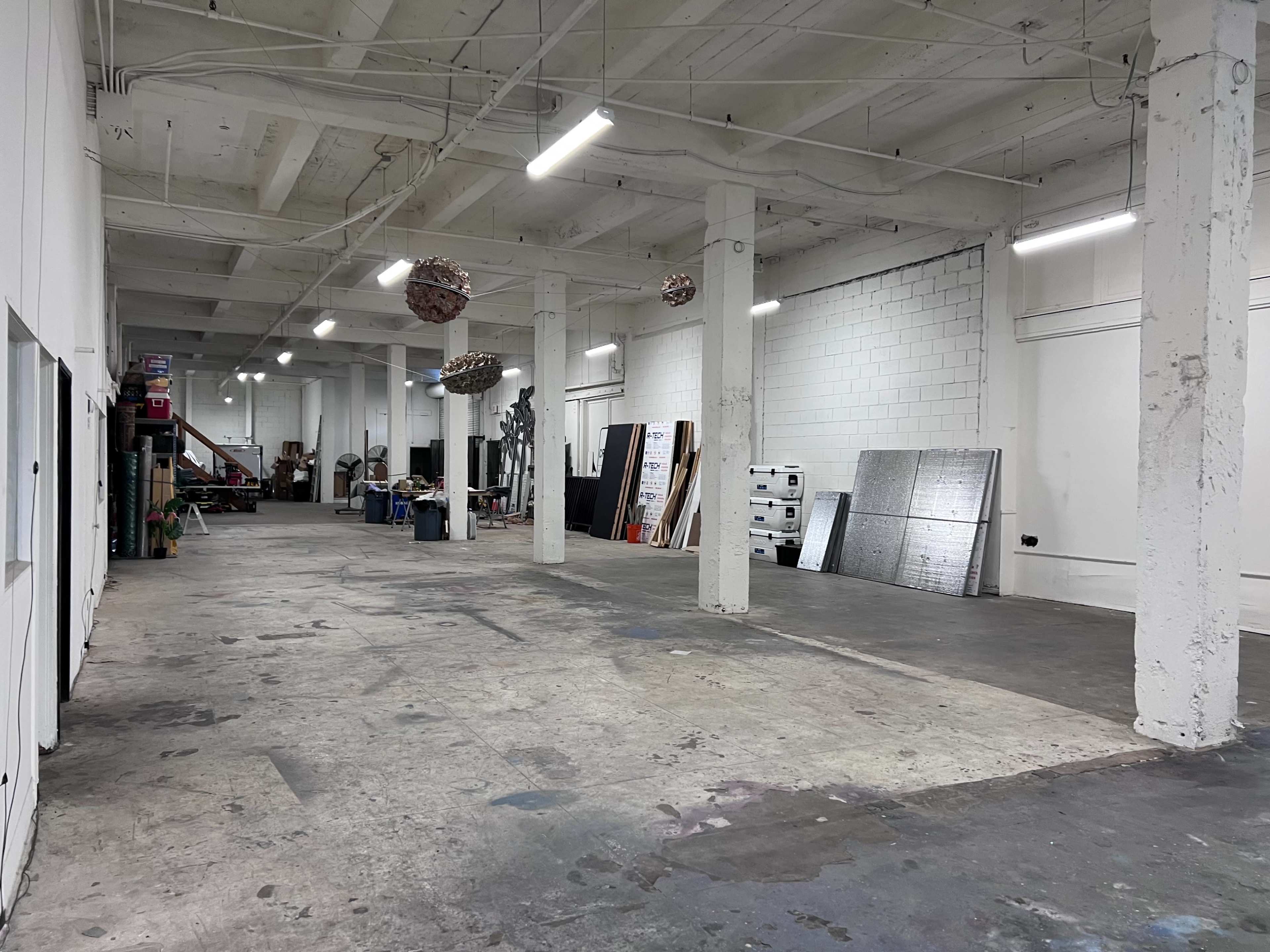 A spacious, empty industrial room with exposed beams, concrete flooring, and various materials and tools scattered along the walls.