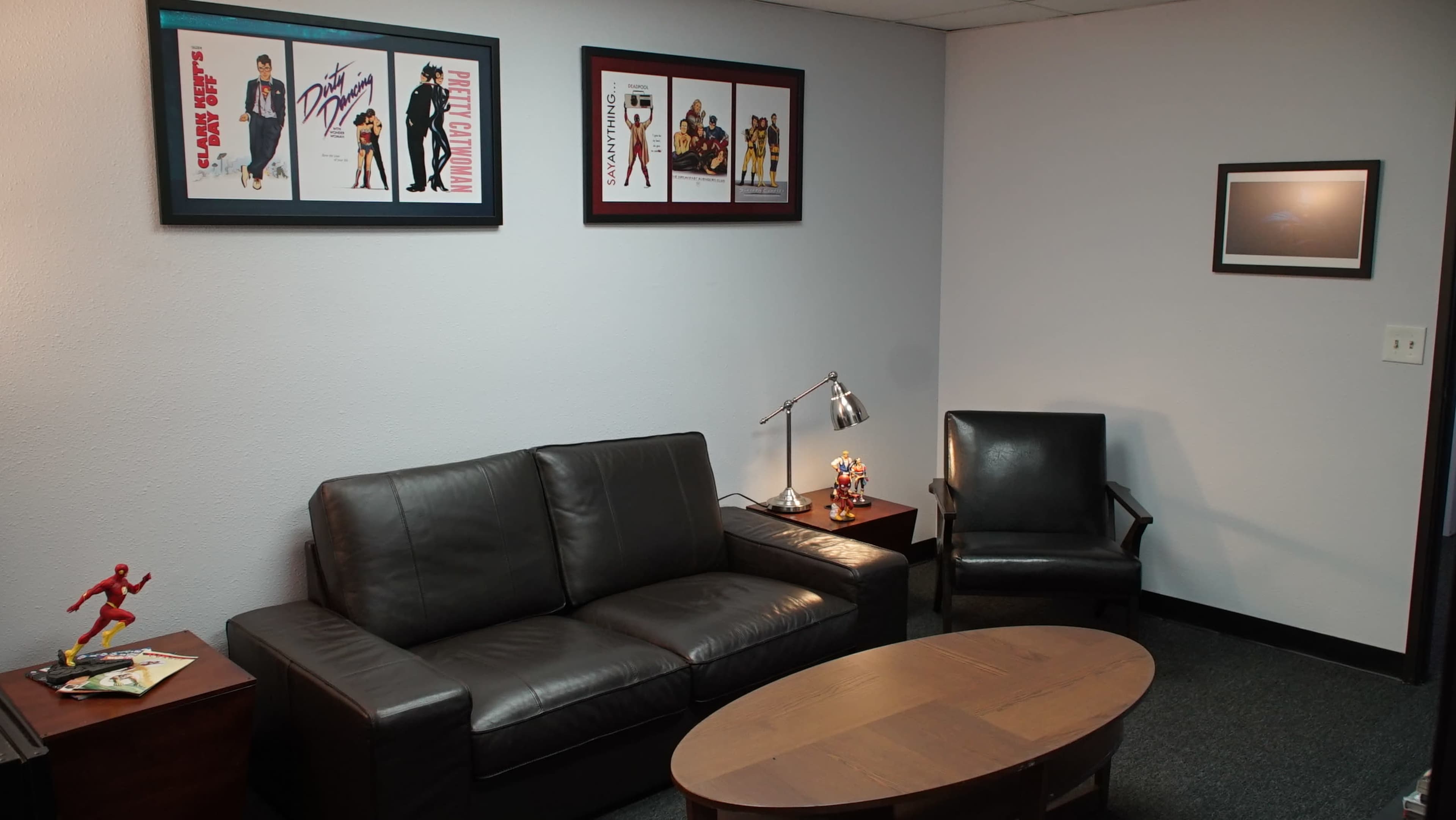 A small waiting area with a dark leather sofa, a black armchair, a wooden coffee table, and framed artwork on the walls.