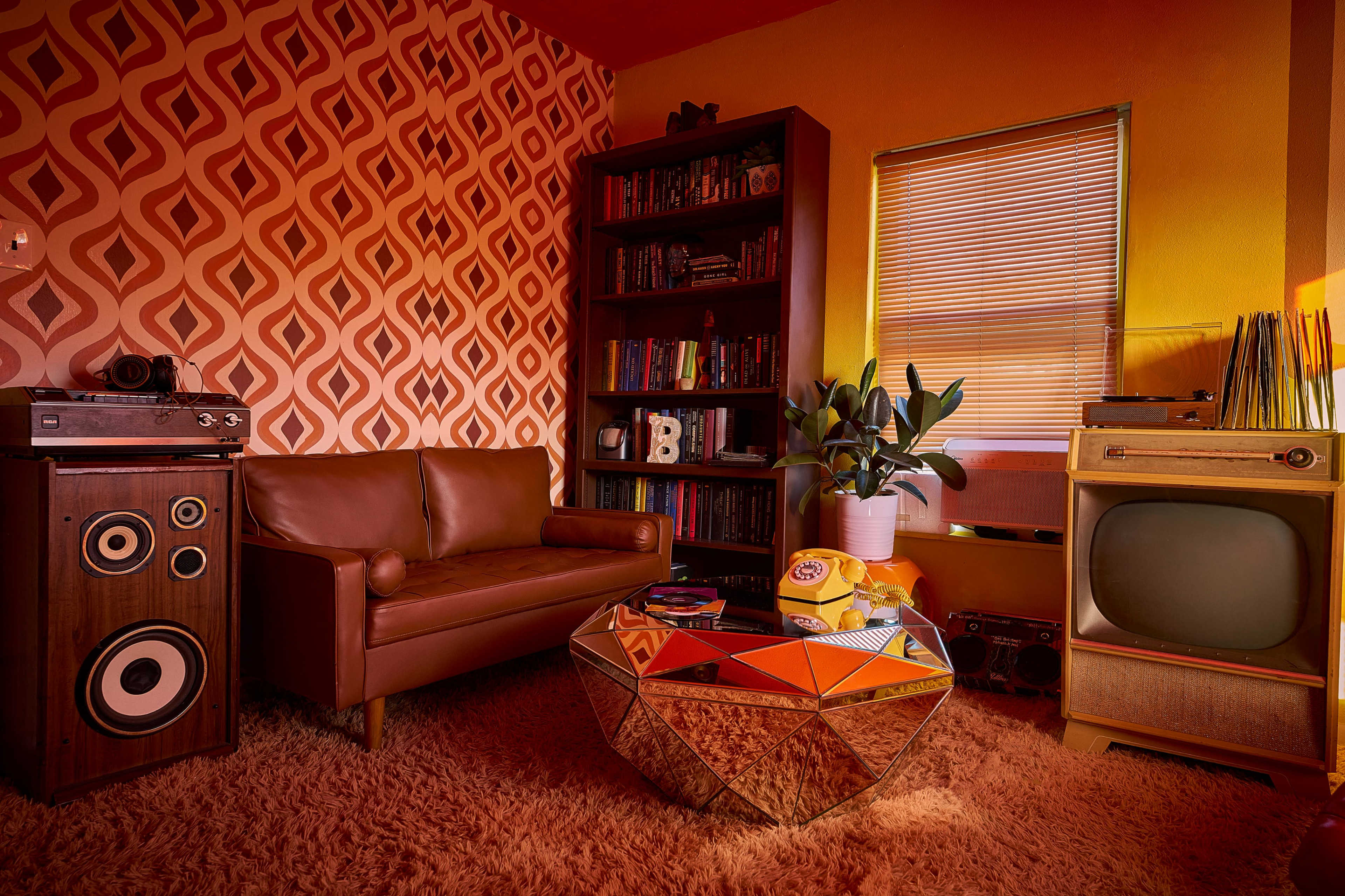 A cozy living room with a brown leather sofa, a vintage television, a bookshelf filled with books, and a geometric coffee table on a plush carpet.