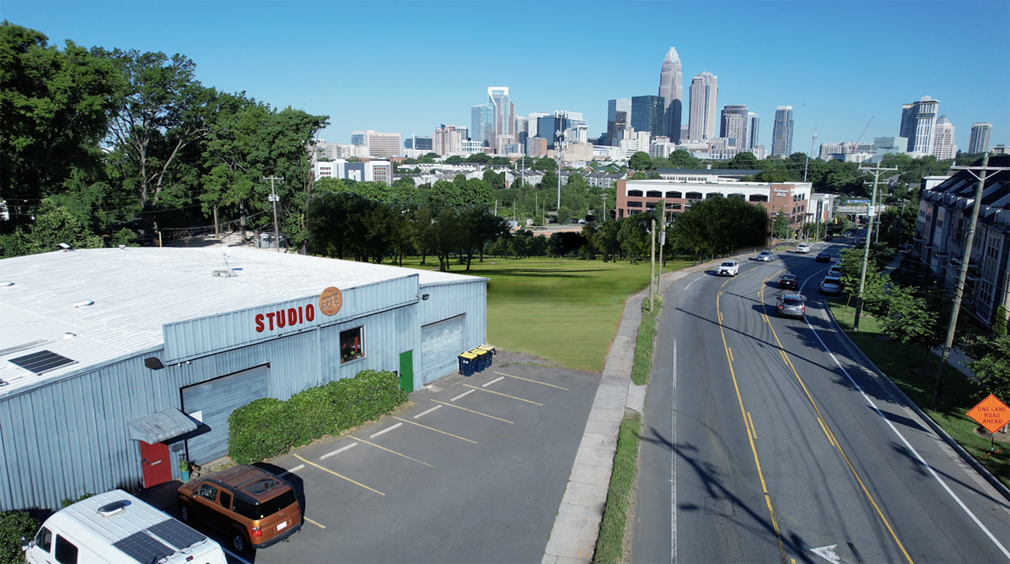 A parking area next to a building labeled "STUDIO," with a clear view of a city skyline in the background and a road running alongside.
