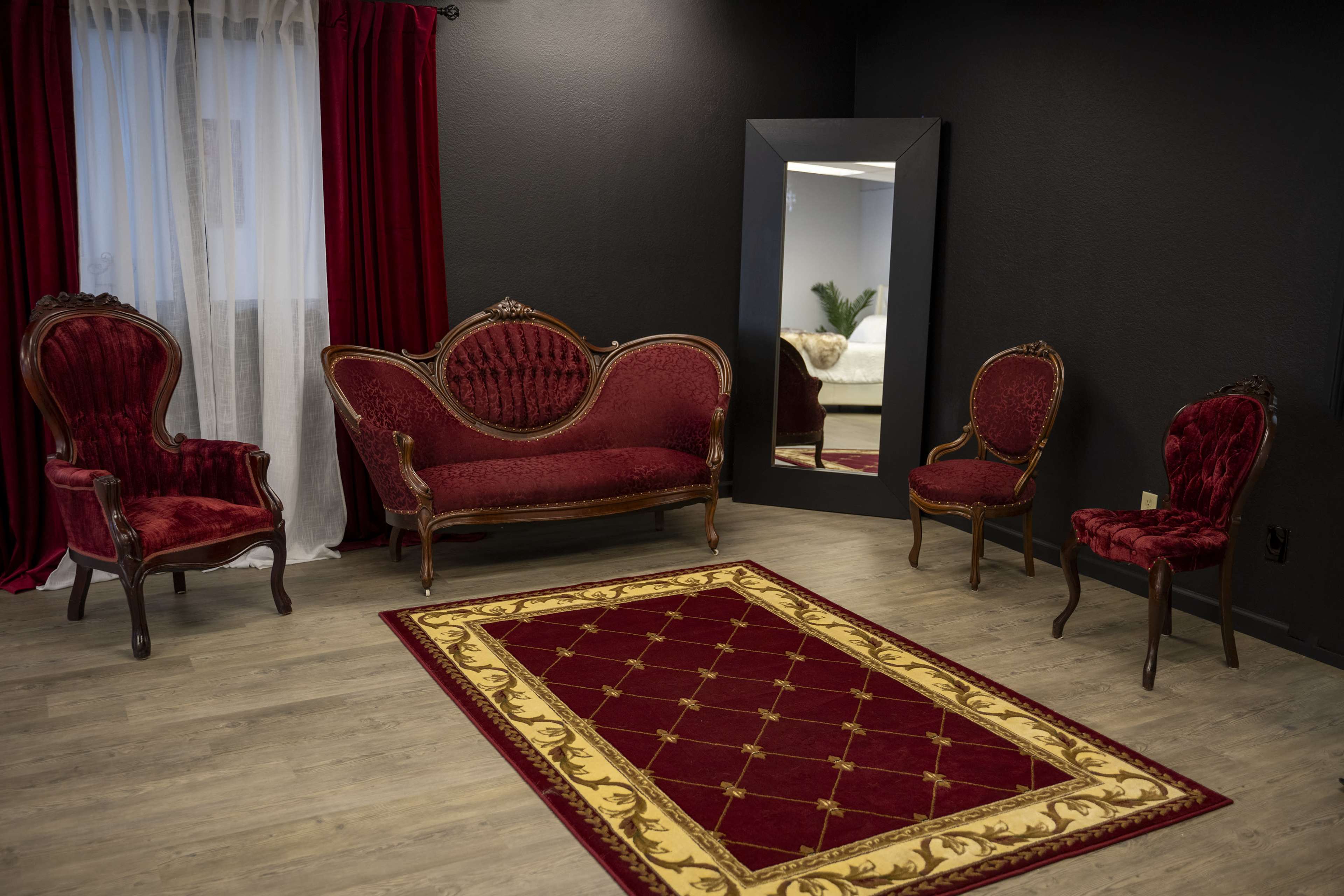 A small room with a red velvet sofa and two matching chairs, arranged around a patterned area rug, with a large mirror on one wall.