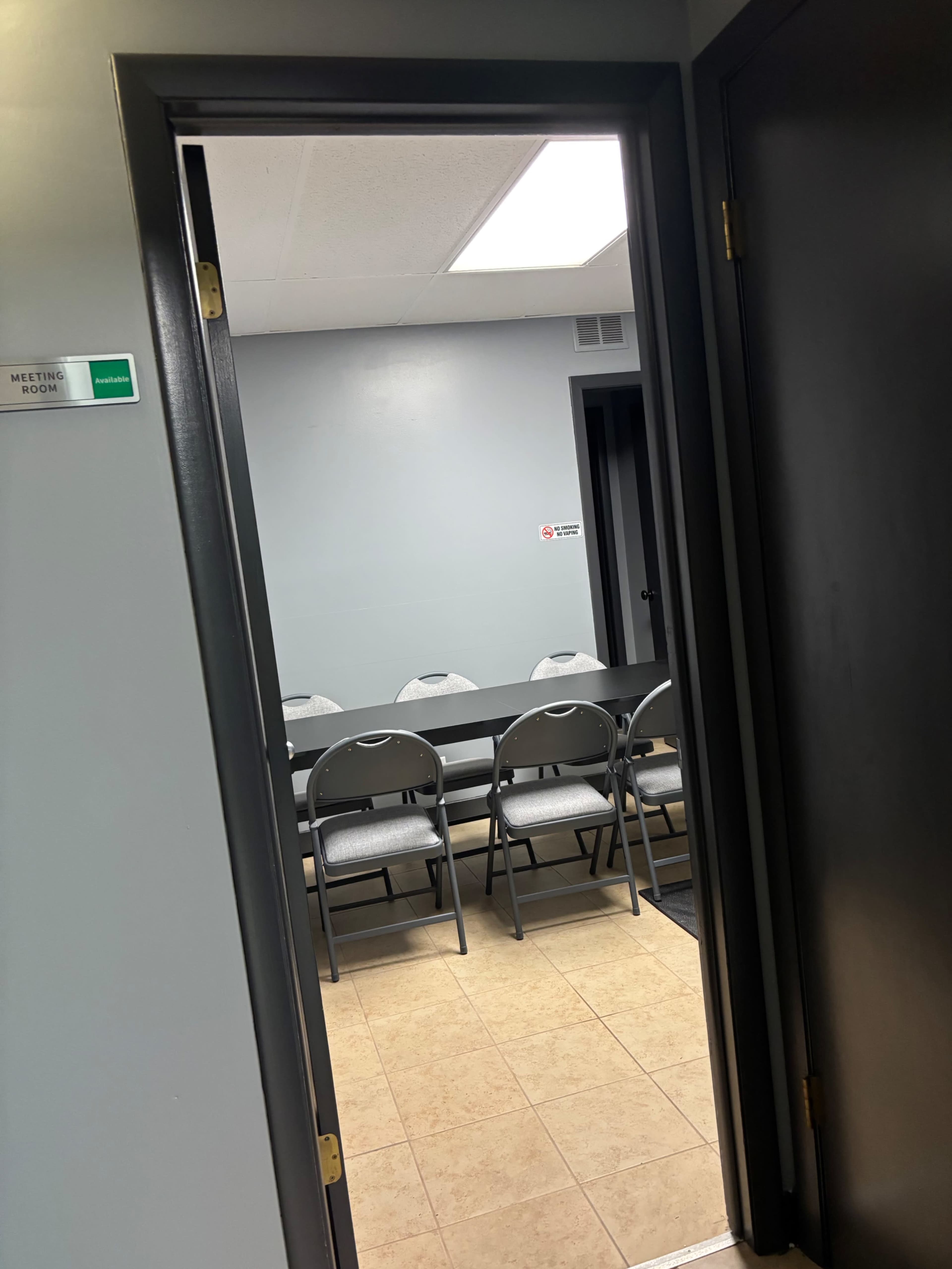 A doorway leads to a meeting room with a long table and several folding chairs arranged around it.