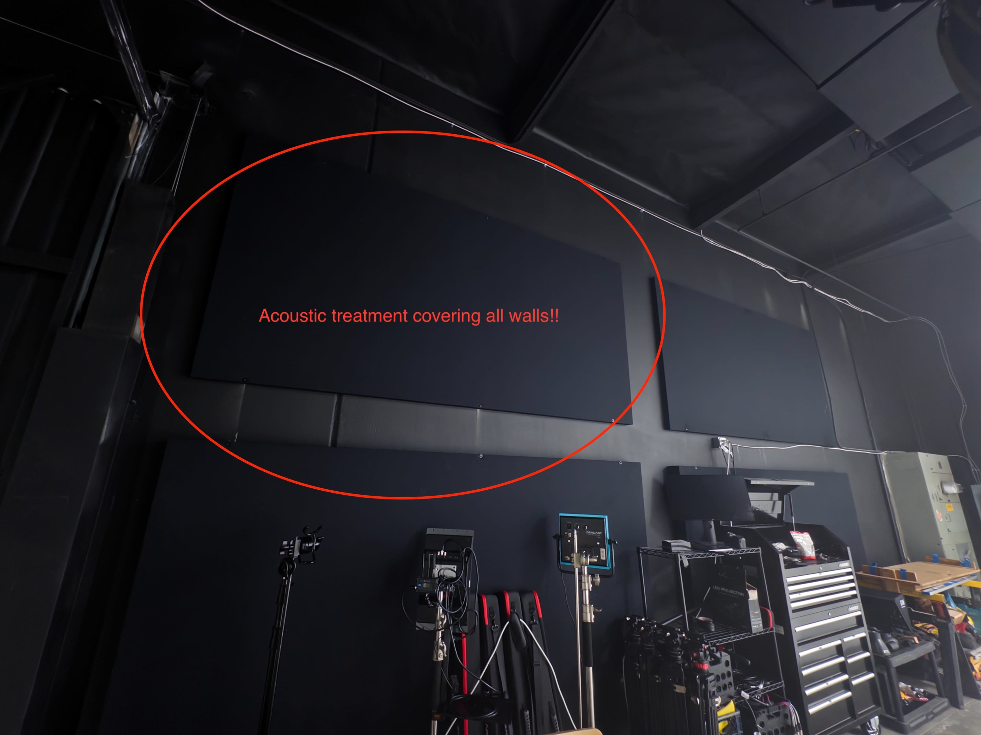 The image shows a studio space with dark acoustic treatment panels covering the walls, along with various equipment and tools visible in the foreground.