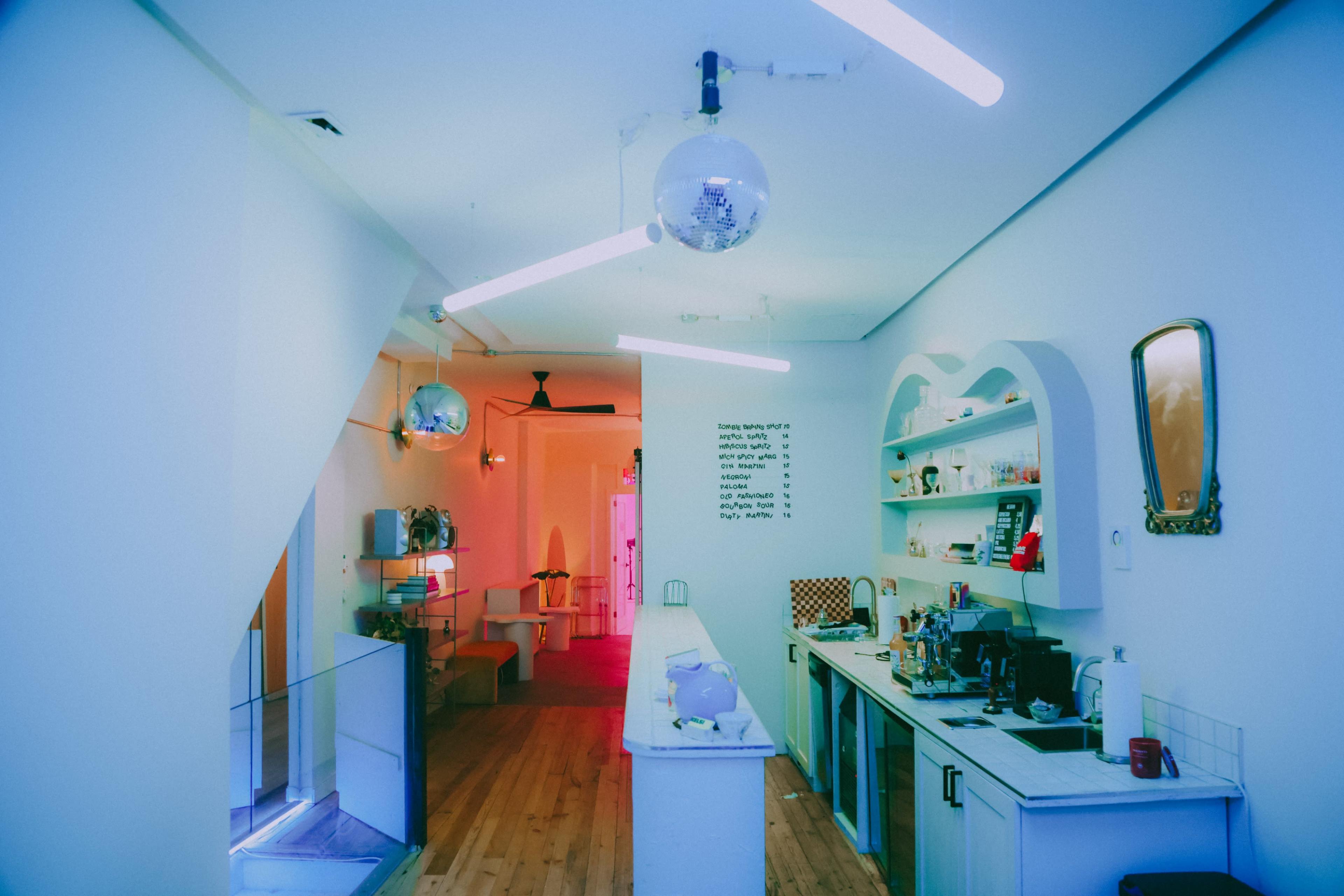 A brightly lit café interior features modern décor, disco balls, and functional kitchen equipment against white walls.