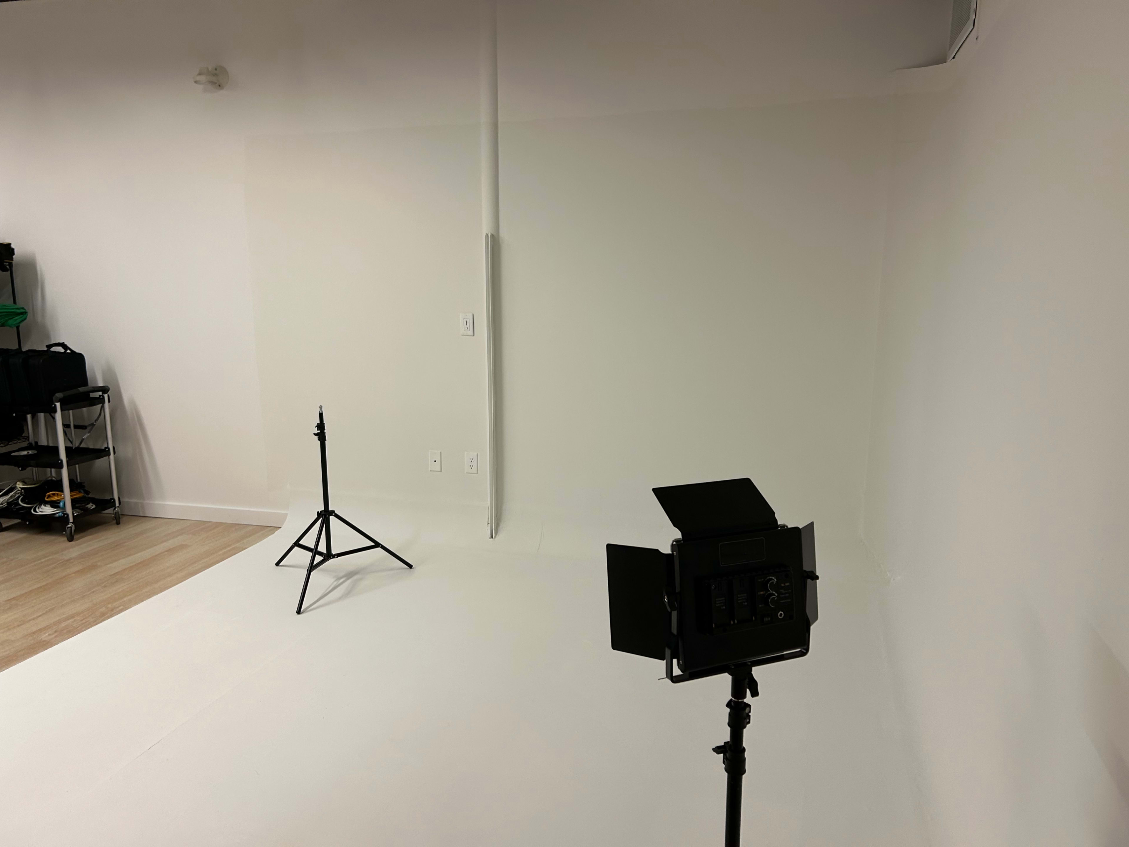 A minimalistic photography studio with a white backdrop, a light stand, and a tripod.