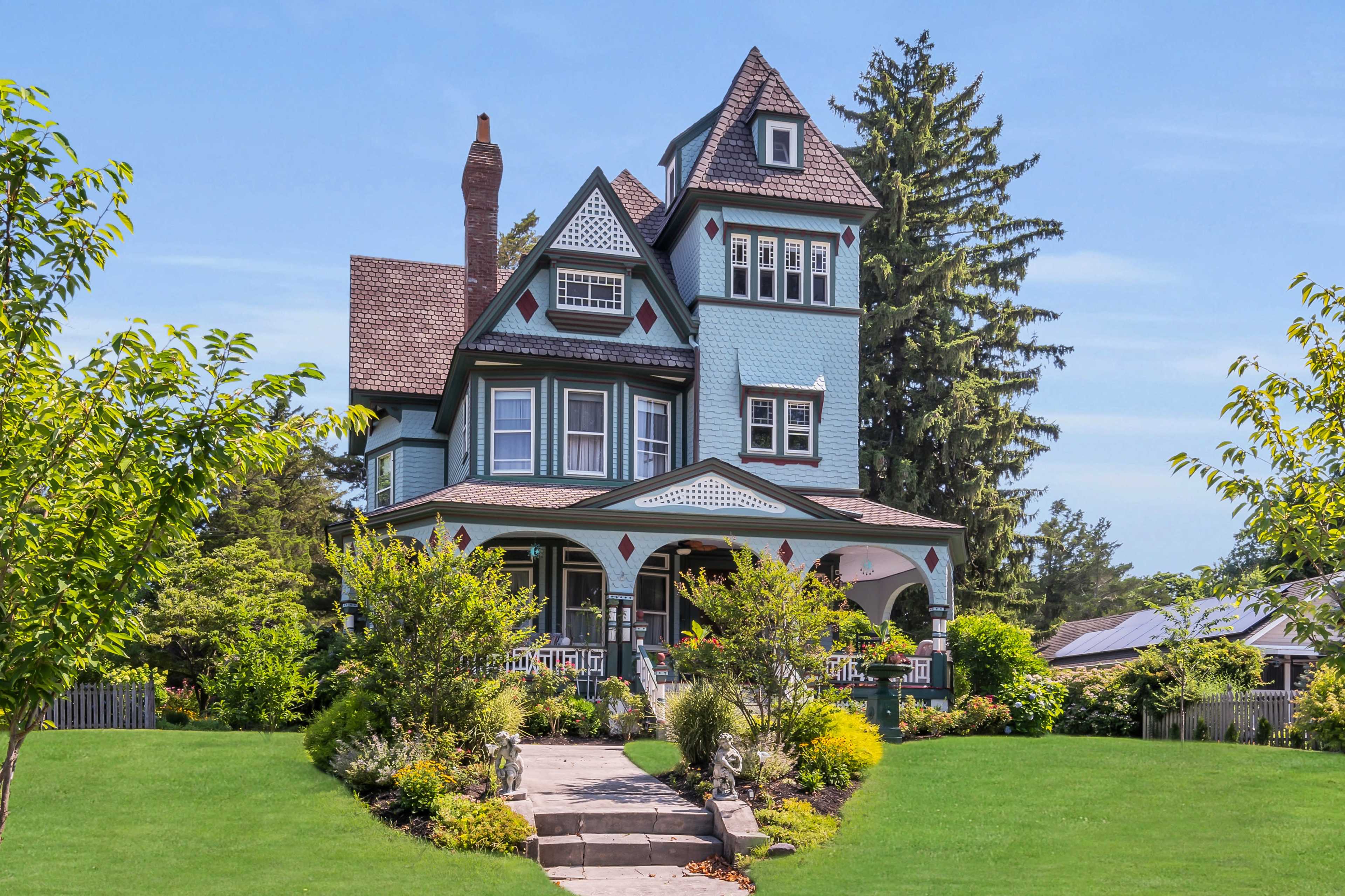 A large, multi-story Victorian-style house surrounded by landscaped gardens and trees.