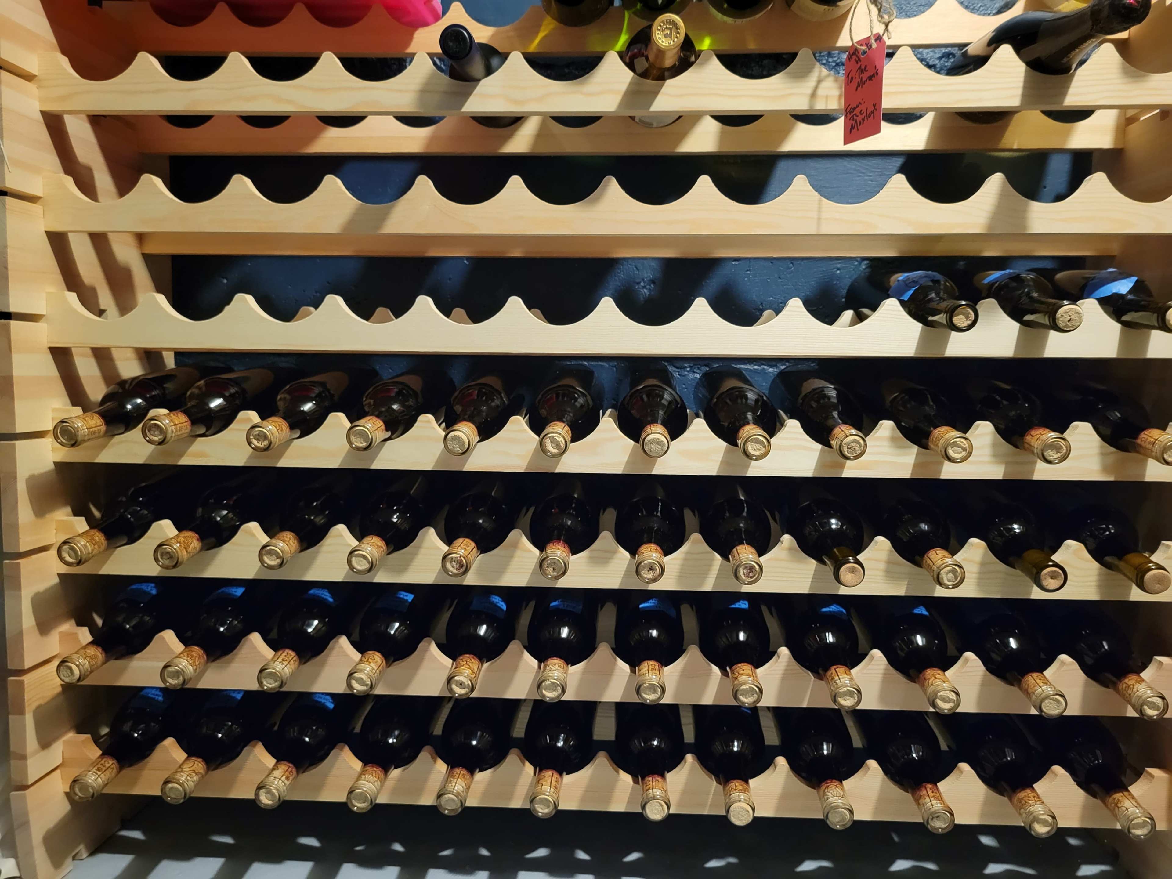 The image shows a wooden wine rack filled with neatly arranged bottles of wine.
