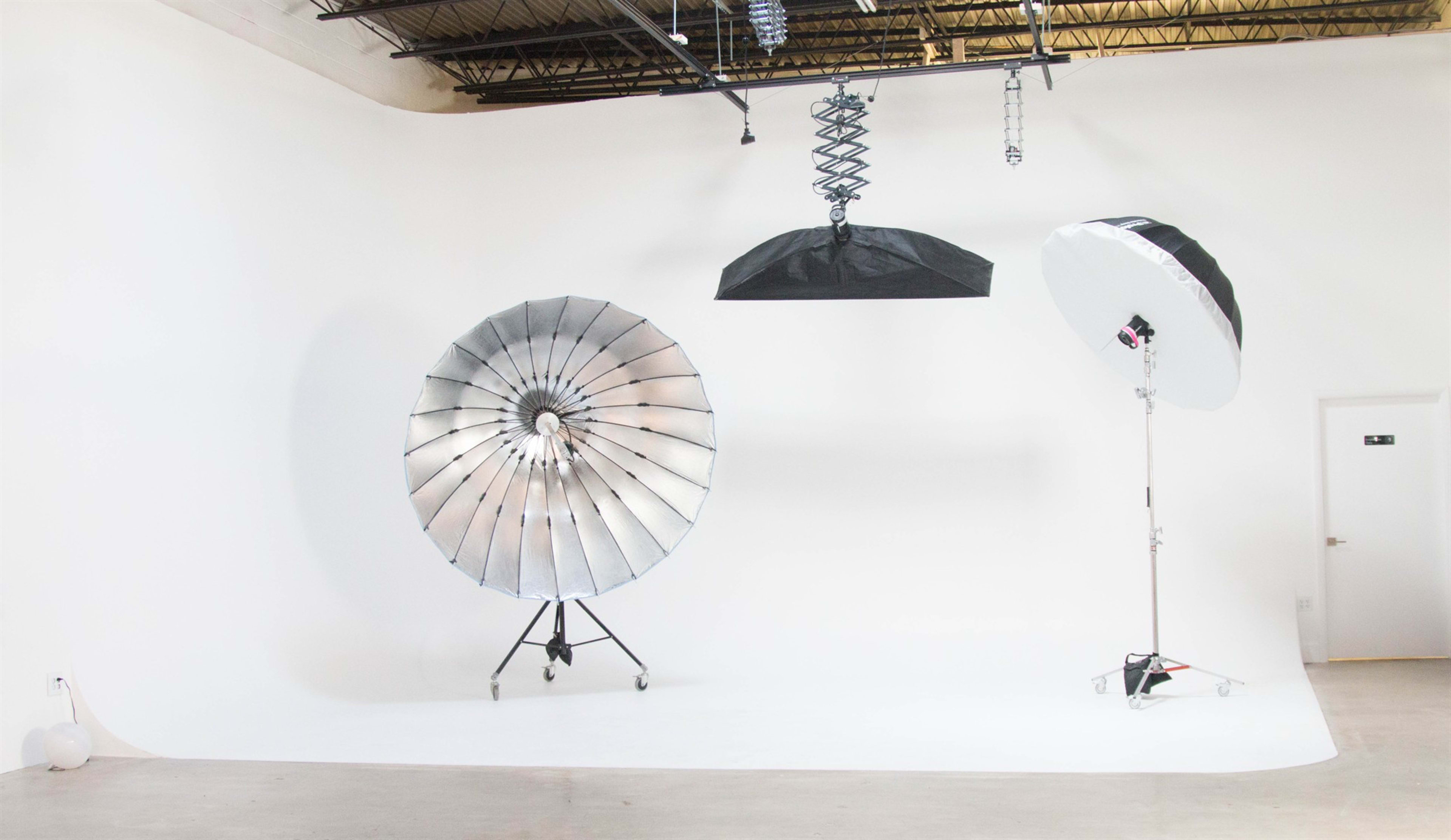 The image shows a photography studio with a large reflector, a softbox, and a roll of seamless paper backdrop.