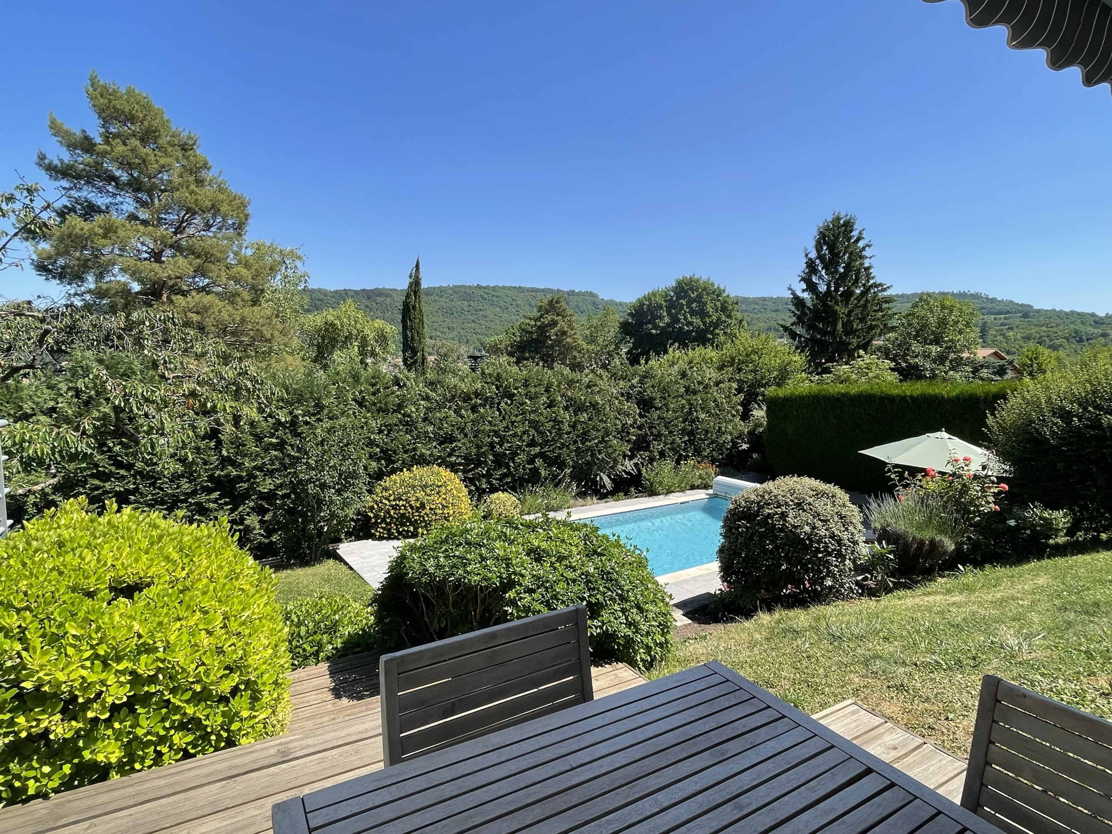 A patio with black outdoor furniture overlooks a swimming pool surrounded by greenery and hills in the background.