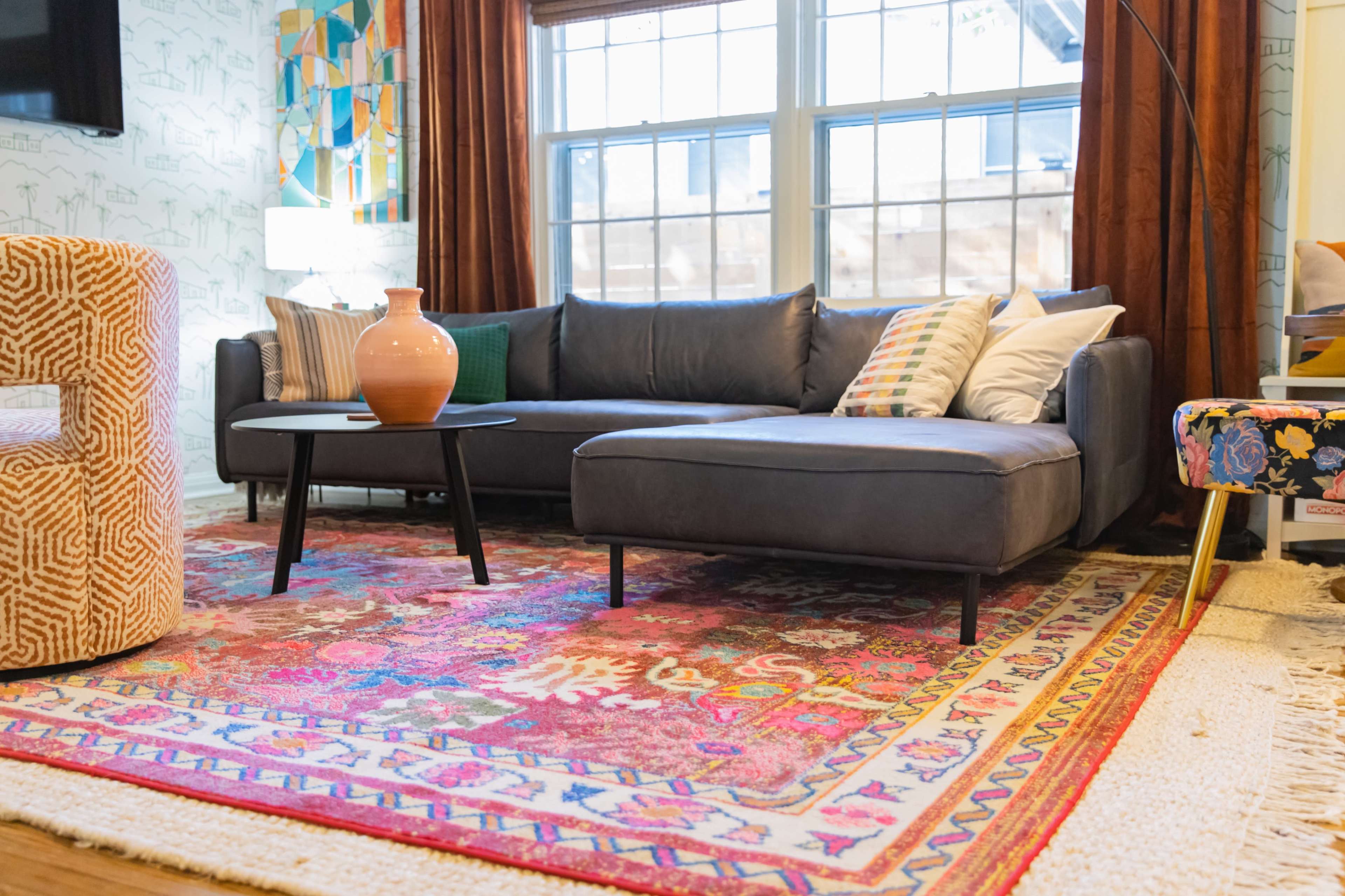 A living room with a dark leather sectional sofa, a round black coffee table, and an intricately patterned area rug beneath them.