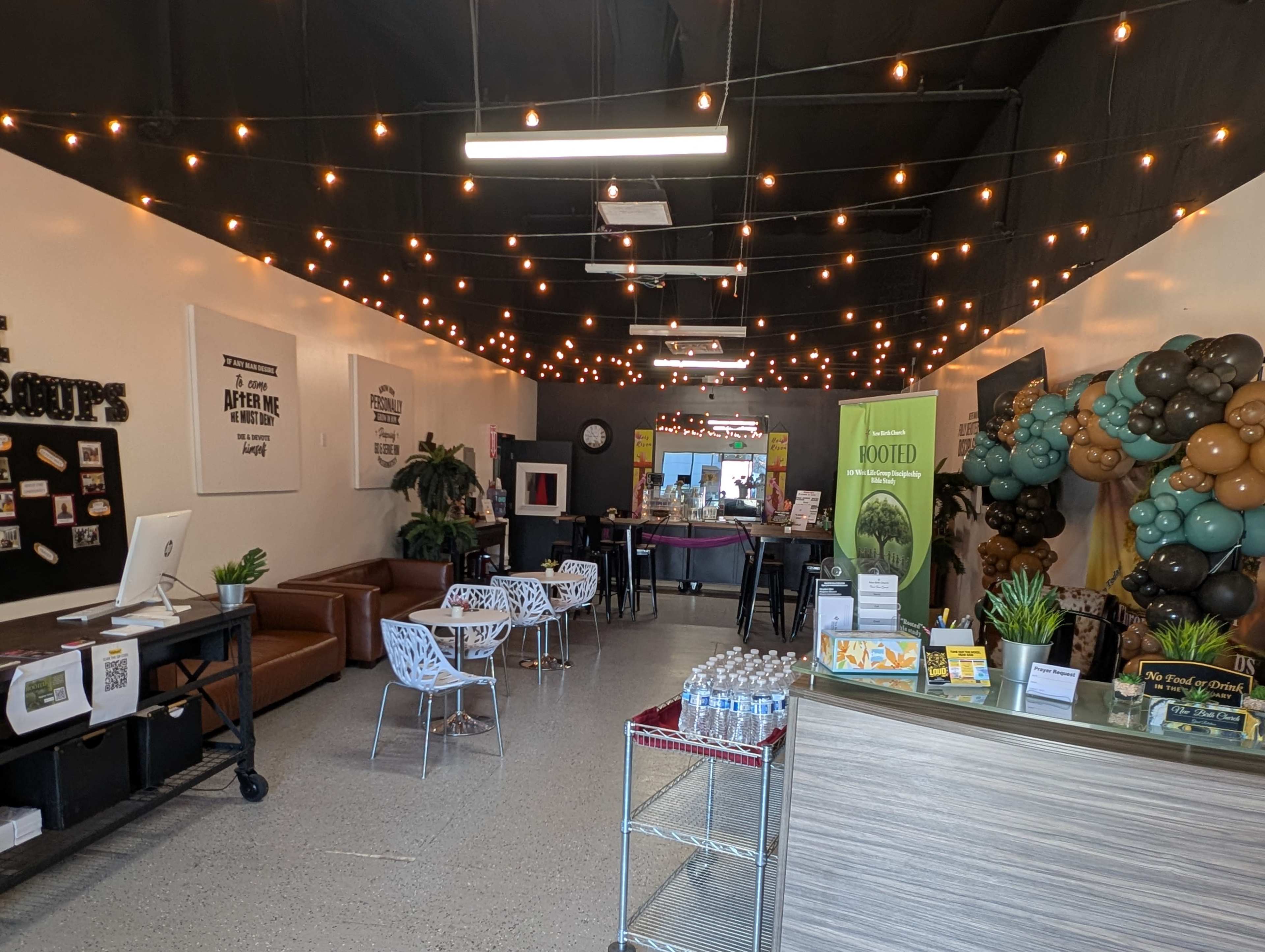 The image shows a vibrant café interior featuring string lights, comfortable seating, a service counter, and a decorated wall with balloons.