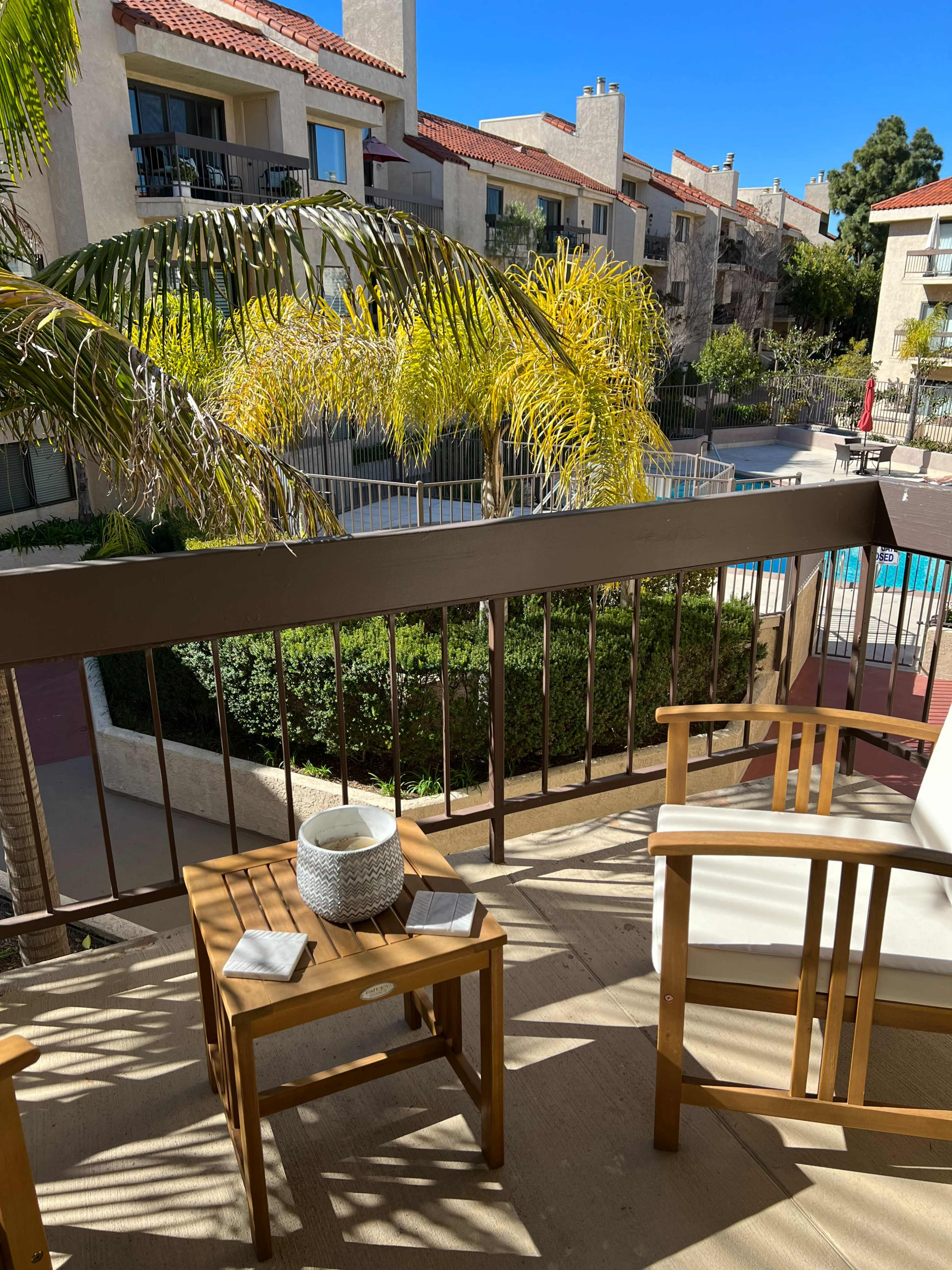 A balcony overlooks a landscaped courtyard with a swimming pool surrounded by apartment buildings.