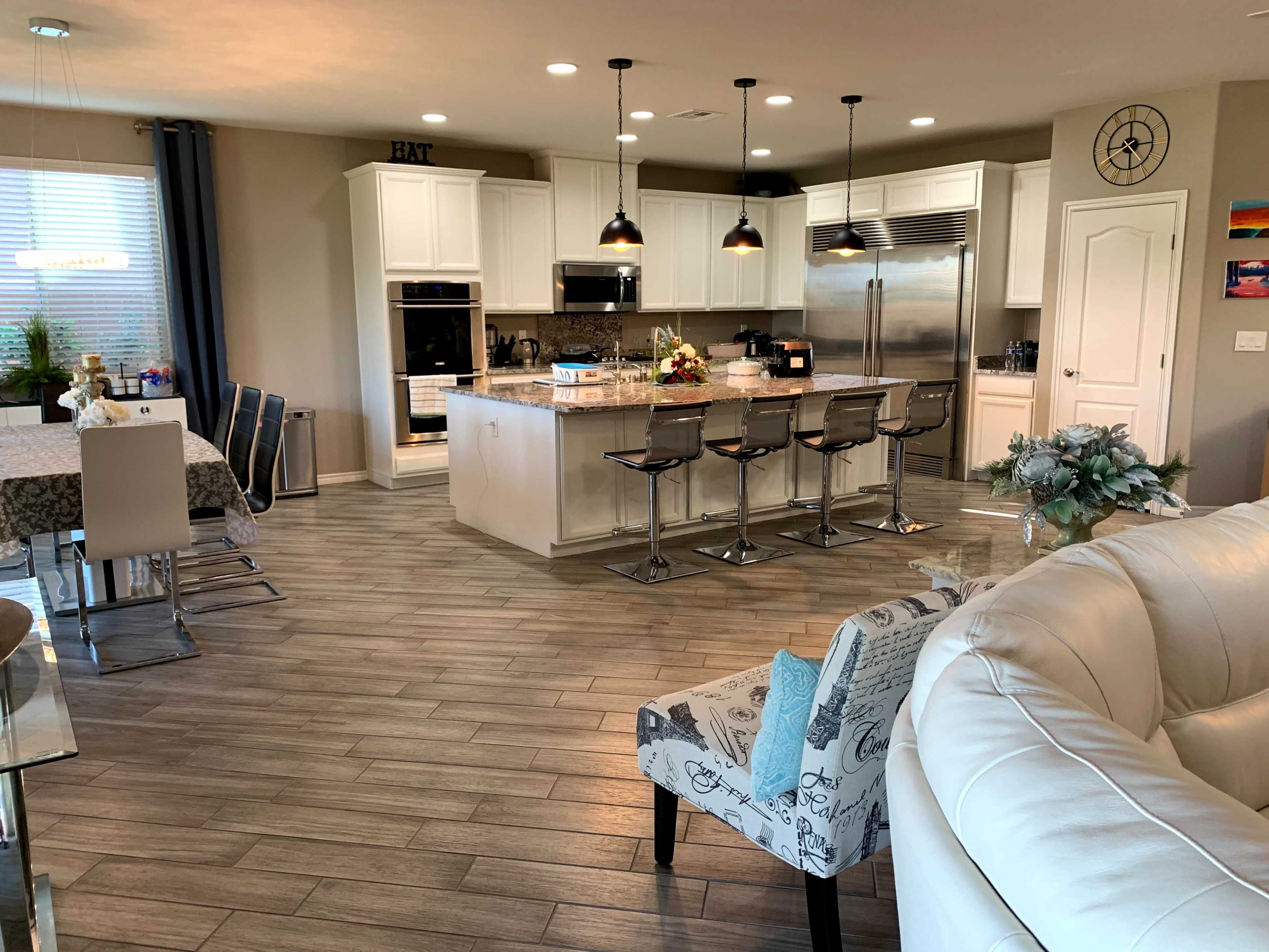 A modern kitchen and dining area featuring a large island with bar stools, a dining table, and light-colored cabinetry.