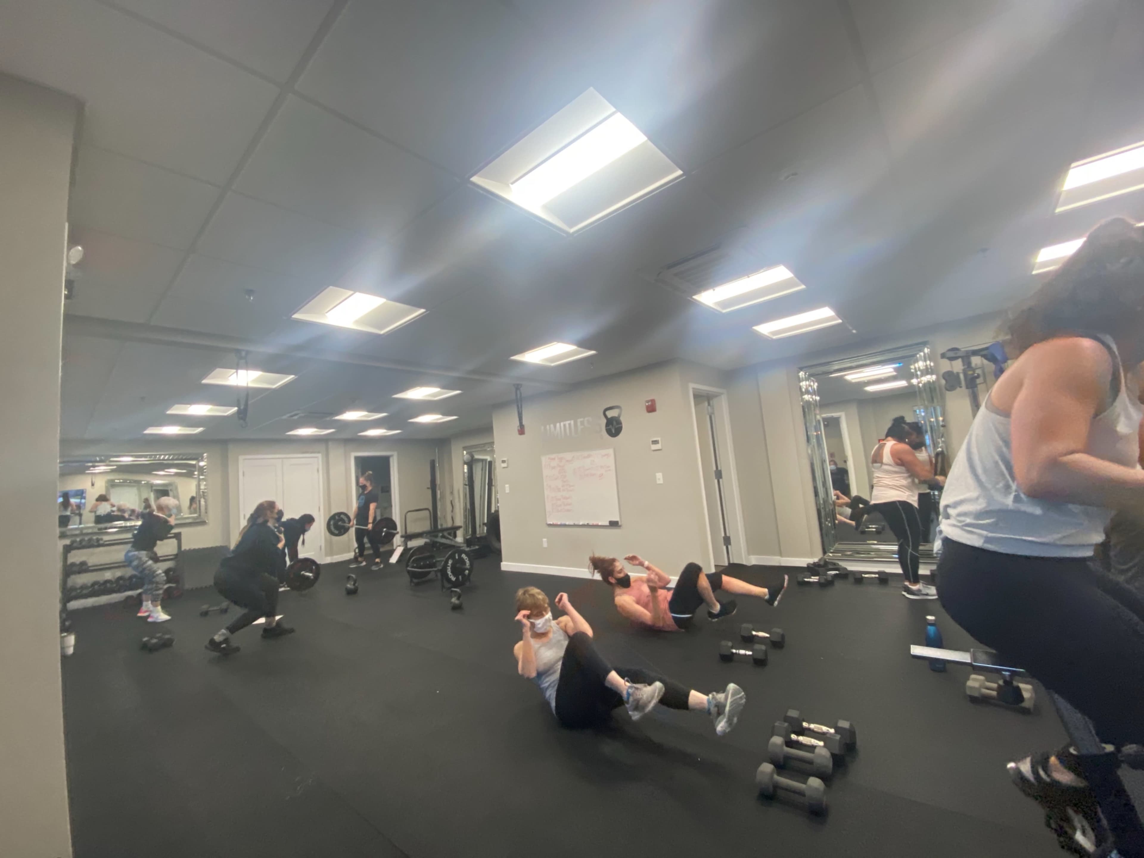 A group of people performs various workout exercises in a fitness studio equipped with weights and exercise mats.