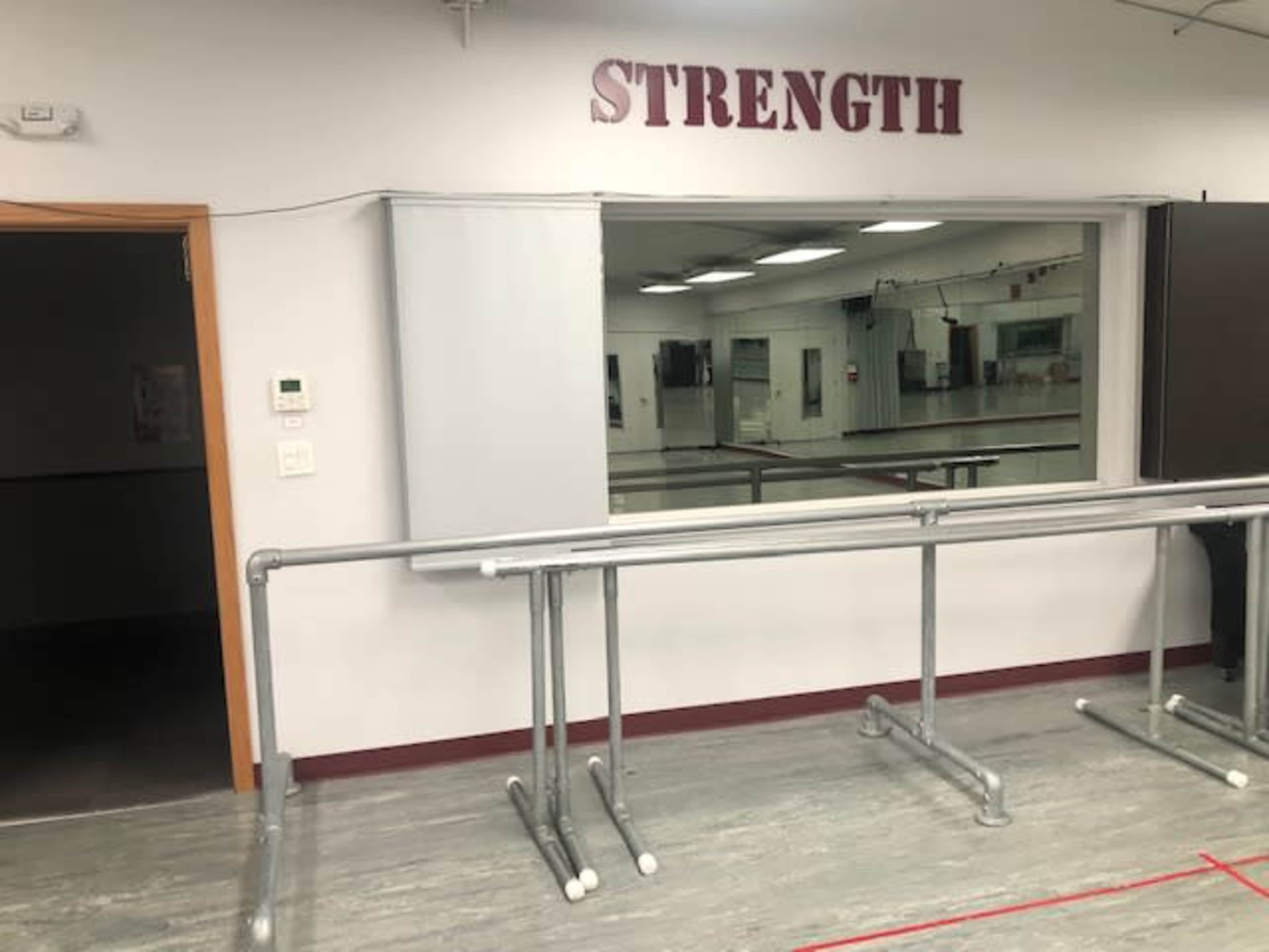 A room with a large mirror, ballet barres, and the word "STRENGTH" displayed on the wall above.