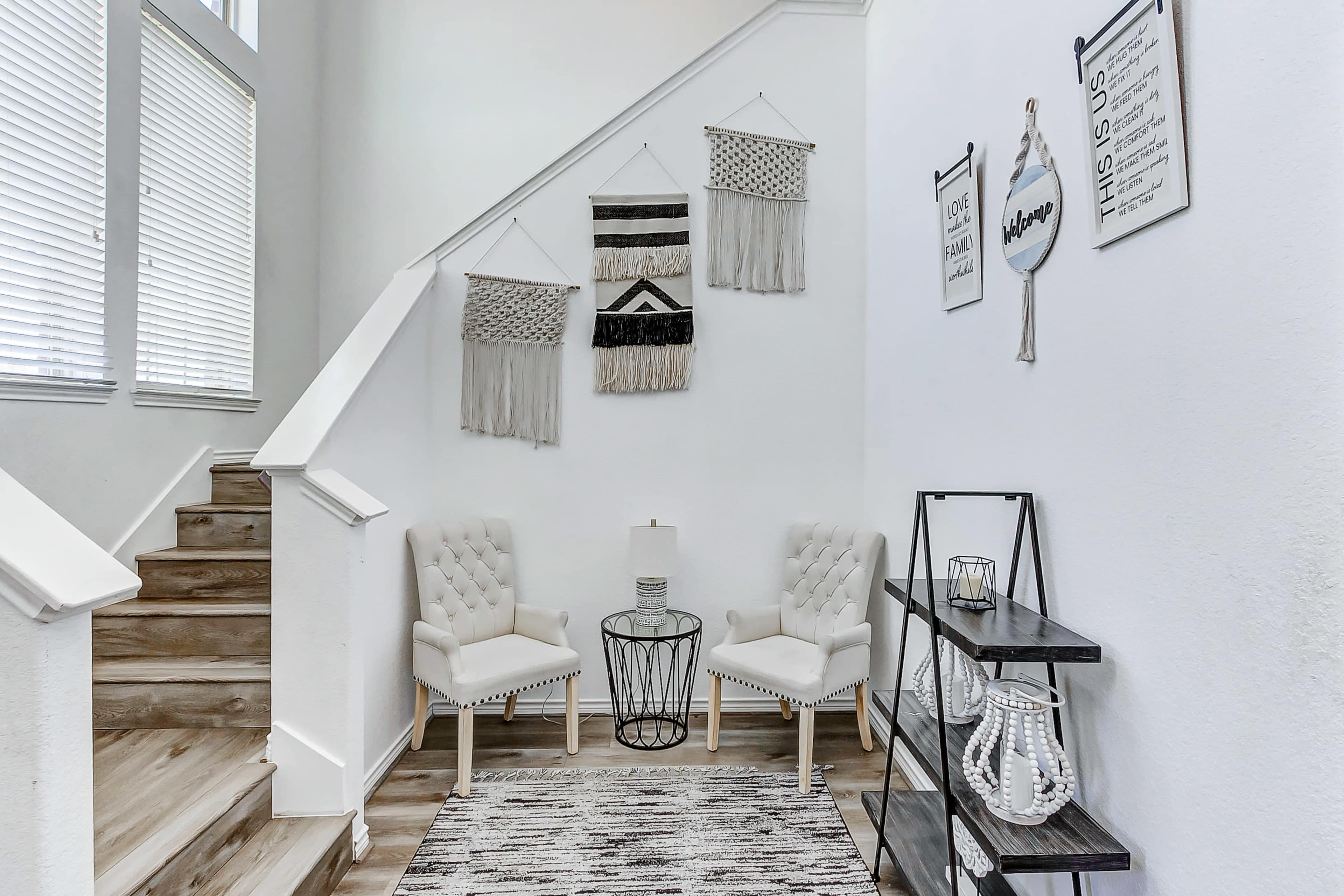 A stairway leads to an inviting corner with two upholstered chairs, a round table, and decorative wall hangings.