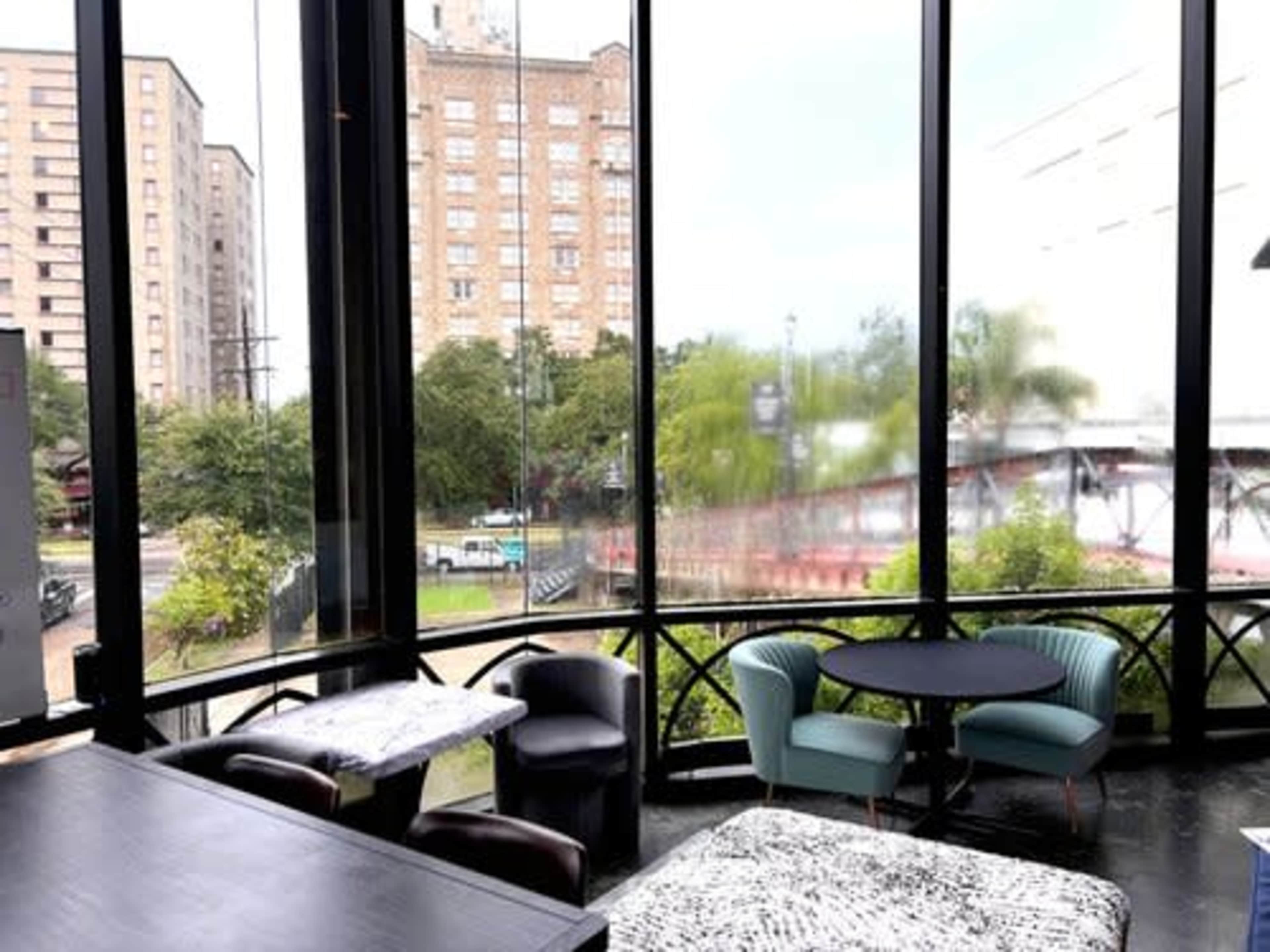 The image shows a modern café interior with large windows, featuring a mix of seating options and a view of a city street with greenery outside.