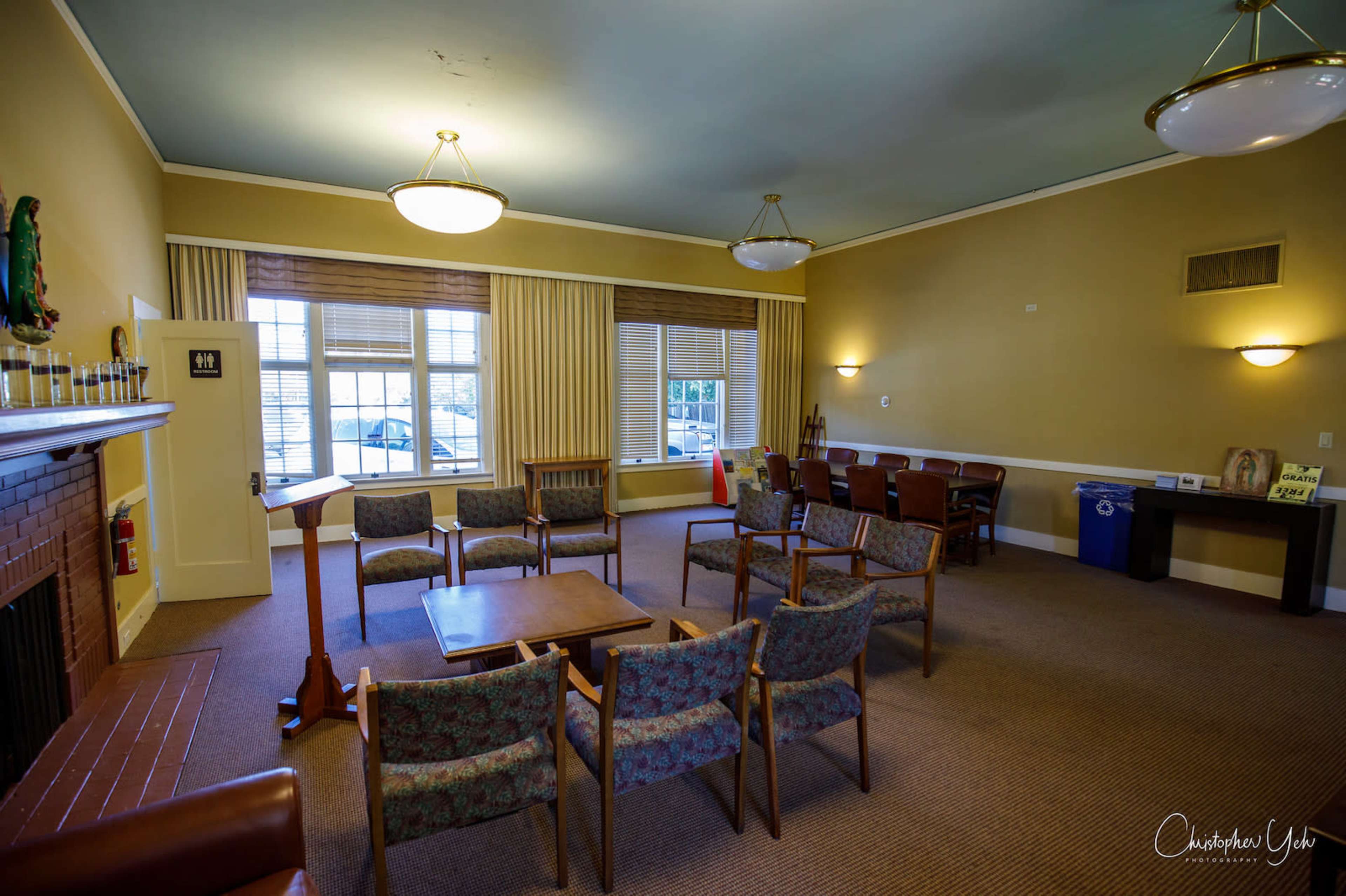 The image shows a spacious room with a seating area, table, and large windows, featuring a fireplace and various furnishings.