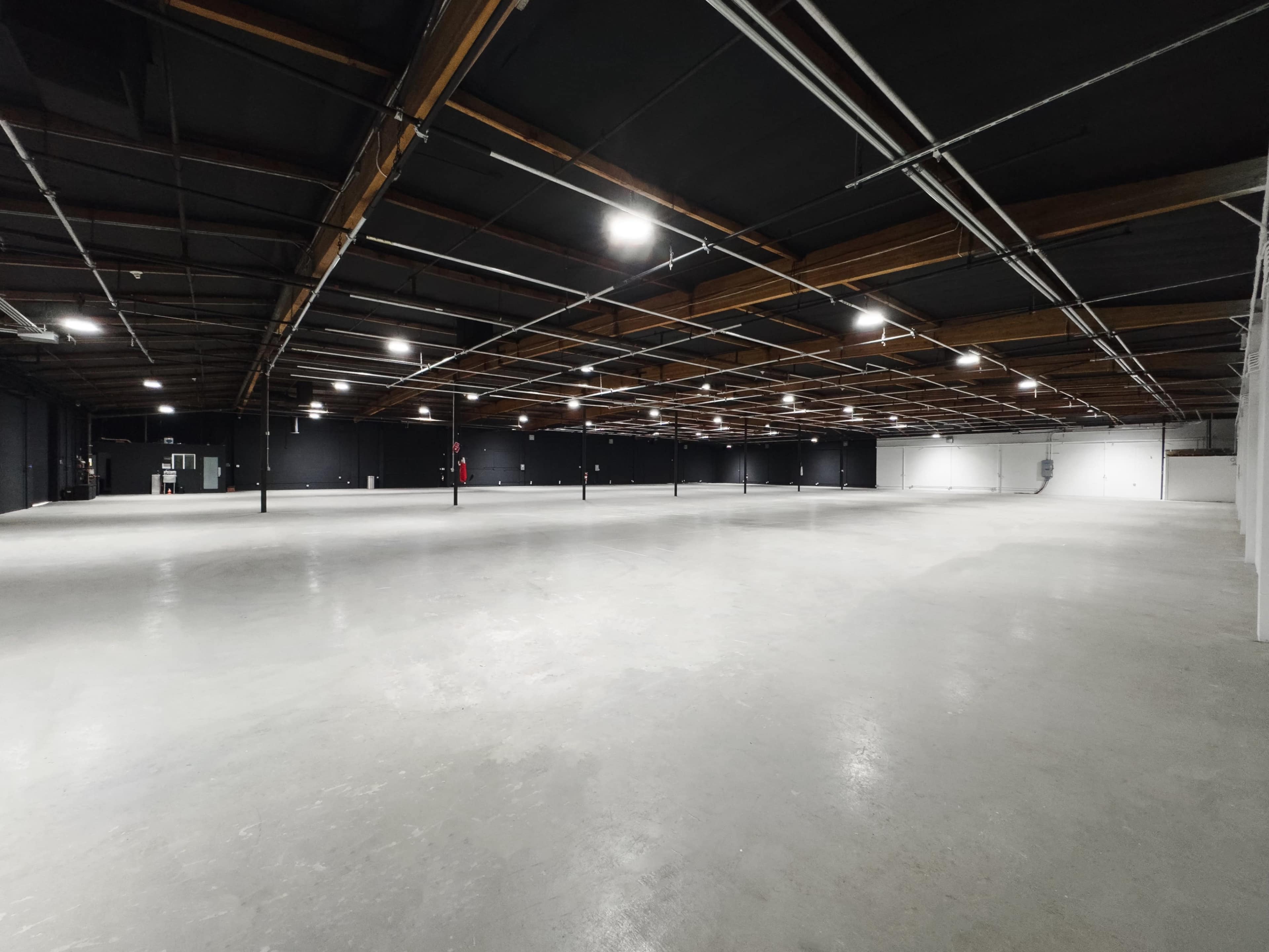 A spacious, empty warehouse with concrete flooring and overhead lighting.